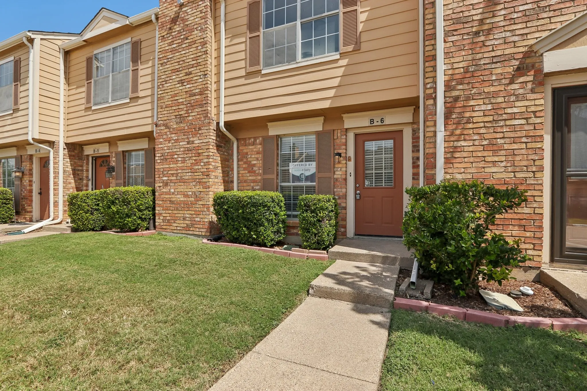 Exterior features include a tan siding facade with brick accents, brown shutters, and a front entry with a glass-paneled door