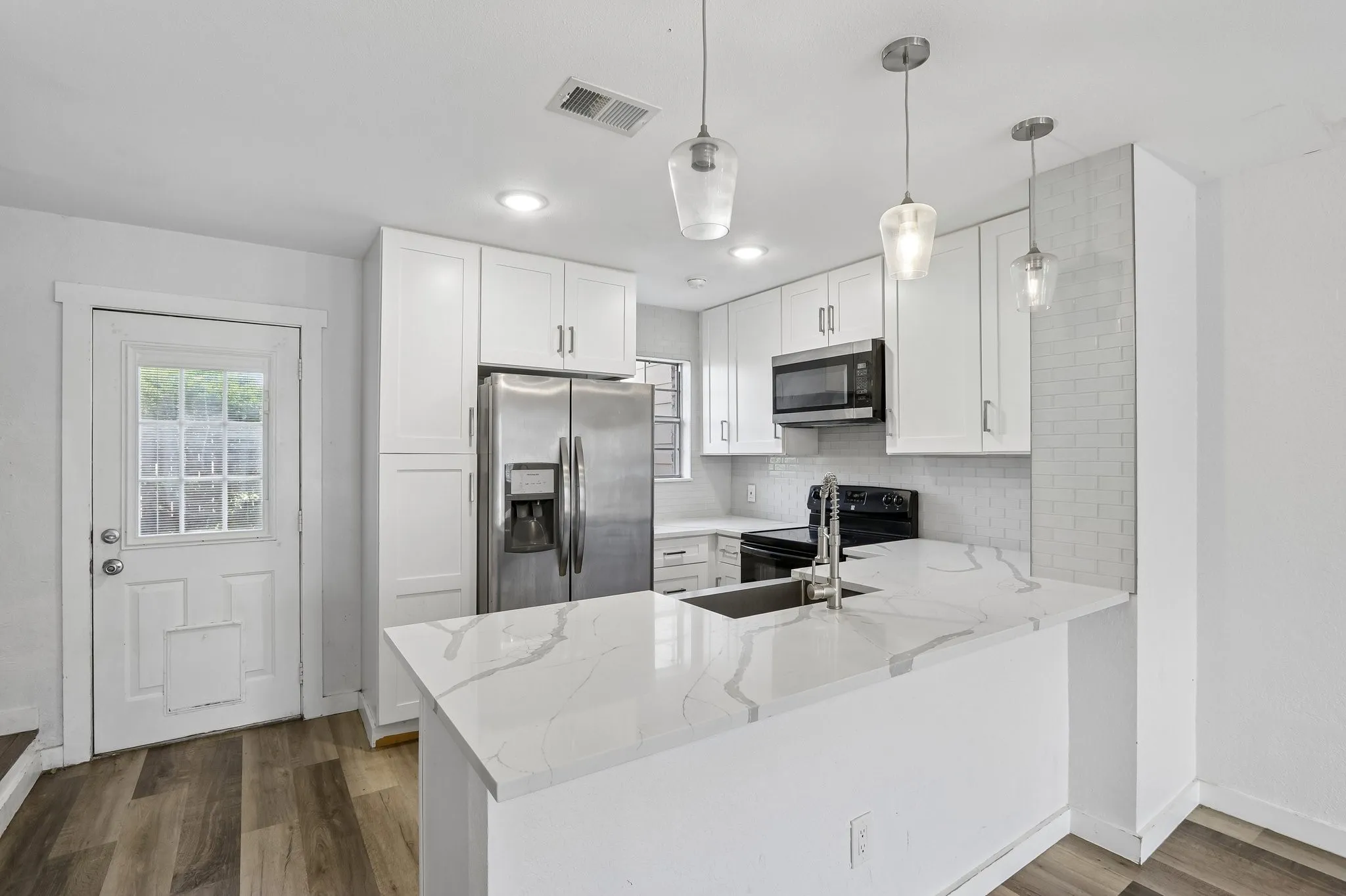 Kitchen featuring white shaker cabinetry, stainless steel appliances, a white patterned countertop, and wood-finish flooring