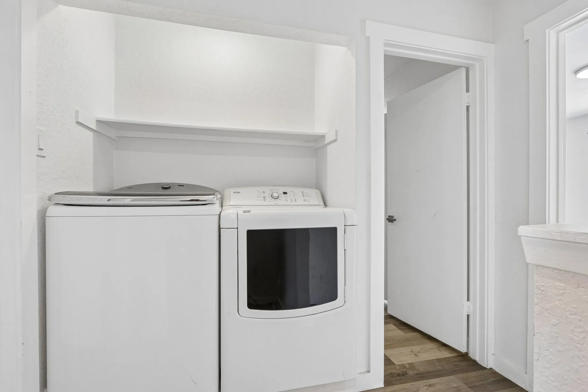 Dedicated laundry area featuring a built-in shelf, white walls, and wood-finish flooring