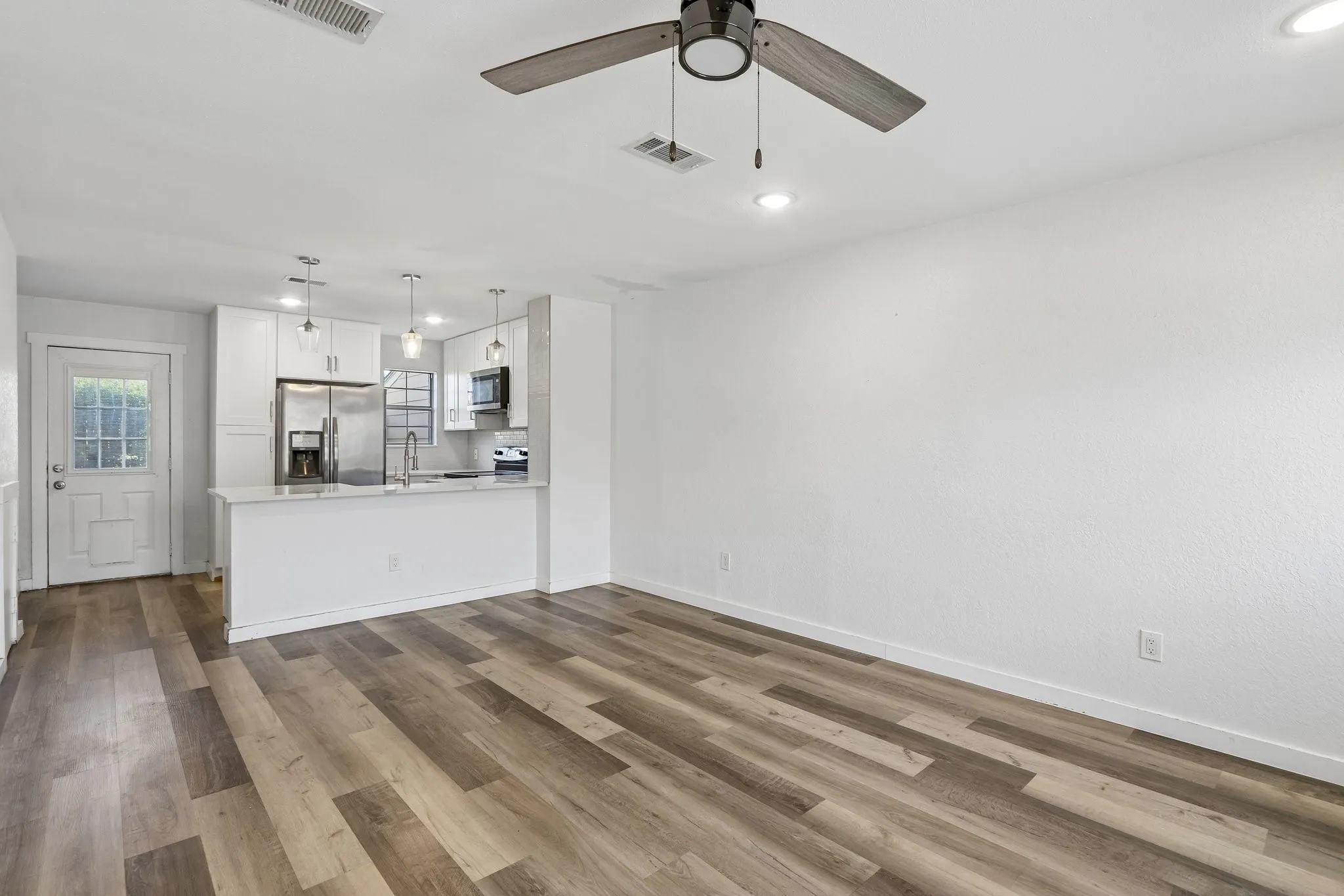 Open-concept living space with wood-finish flooring, a modern ceiling fan, and recessed lighting