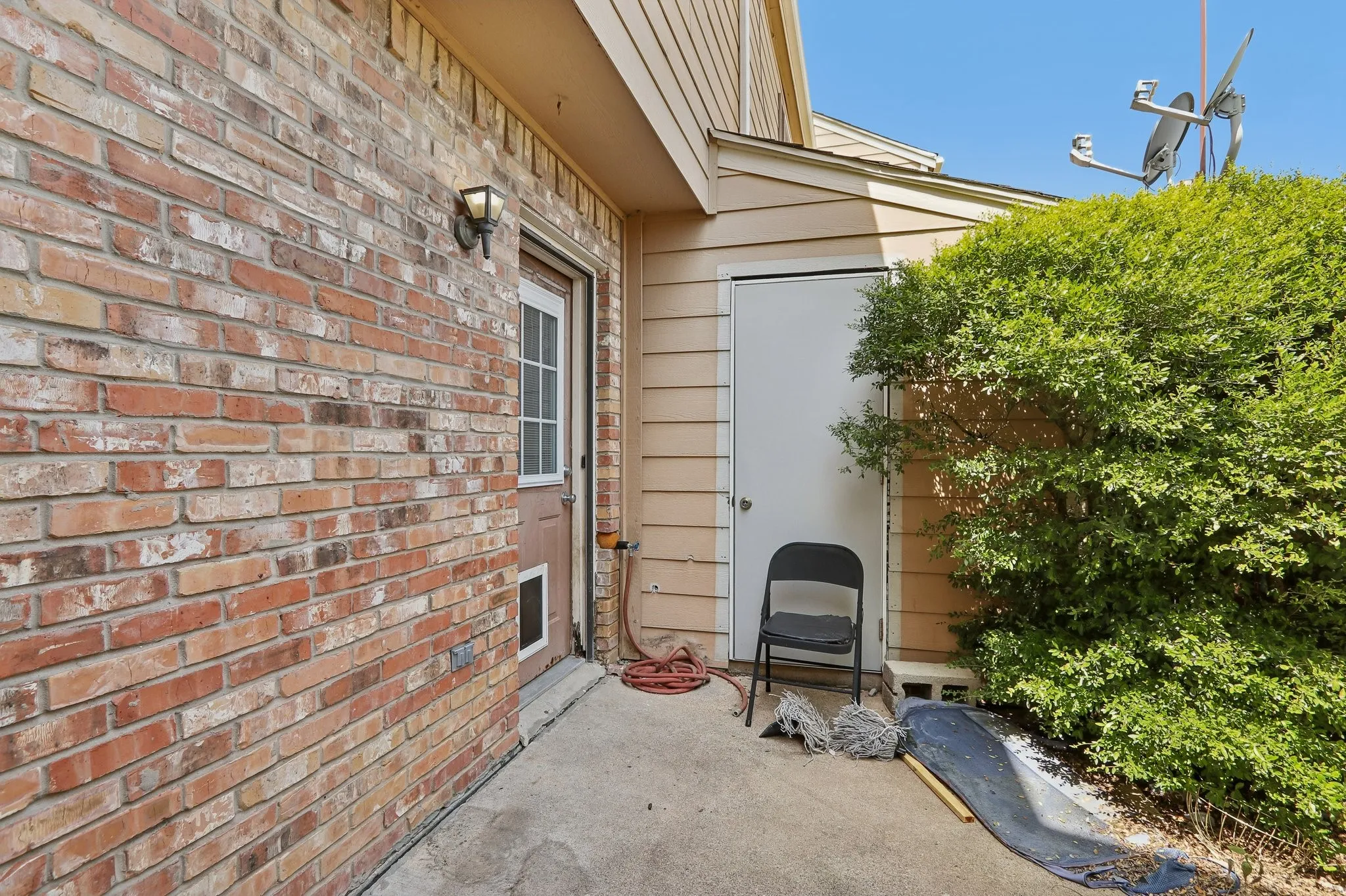 Exterior patio featuring a brick facade, transom window door, and manicured shrubbery