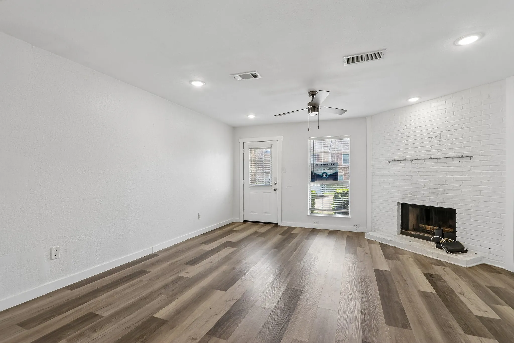 Spacious room featuring wood-finish flooring, a white brick fireplace, recessed lighting, and a ceiling fan