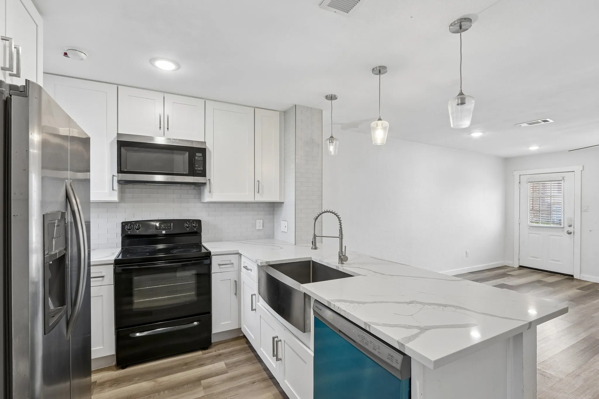 Modern kitchen featuring white shaker cabinetry, stainless steel appliances, white subway tile backsplash, and a large island with a farmhouse sink and pendant lighting