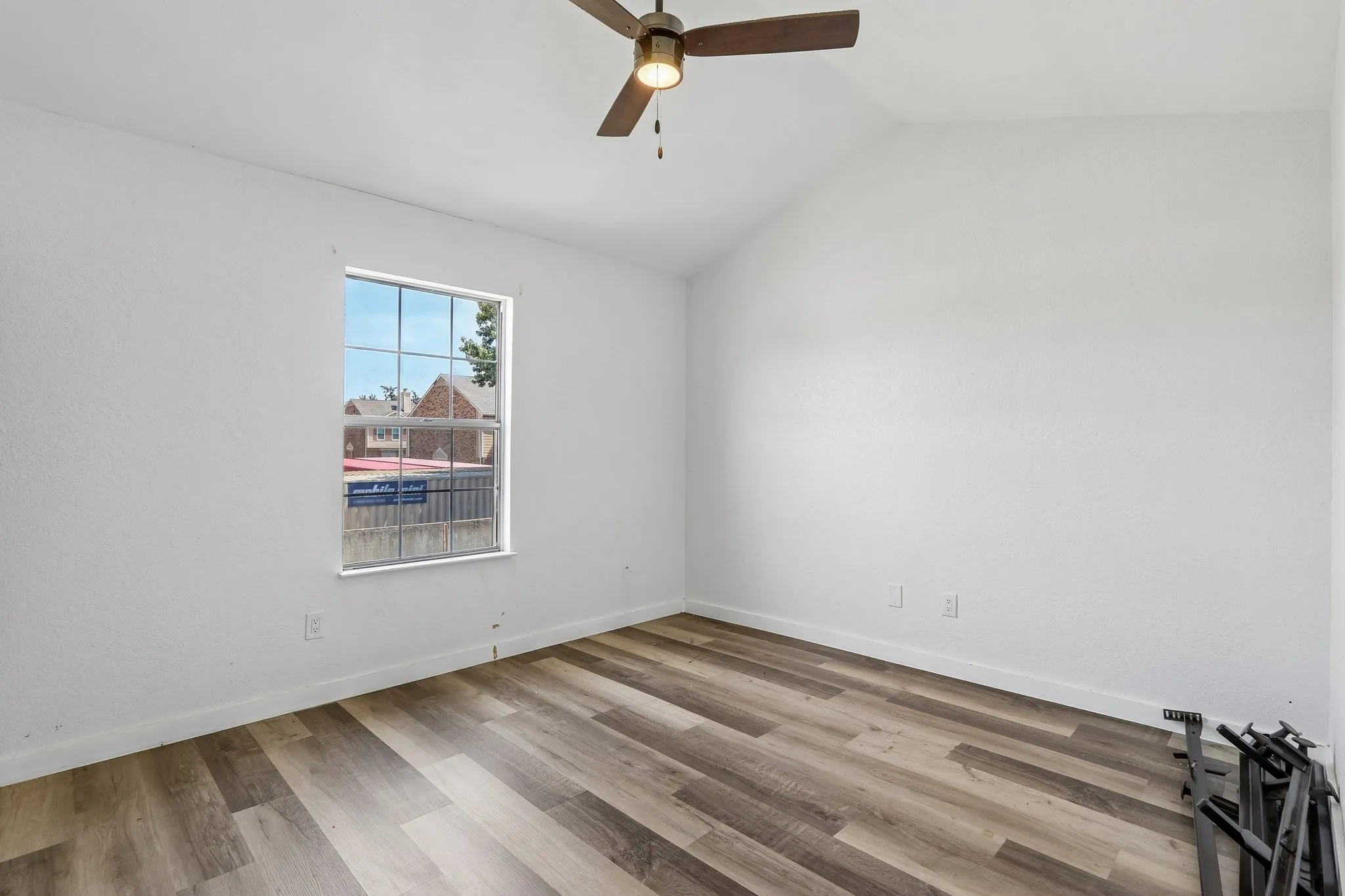 Vaulted ceiling with a ceiling fan, wood-finish flooring, and a multi-pane window