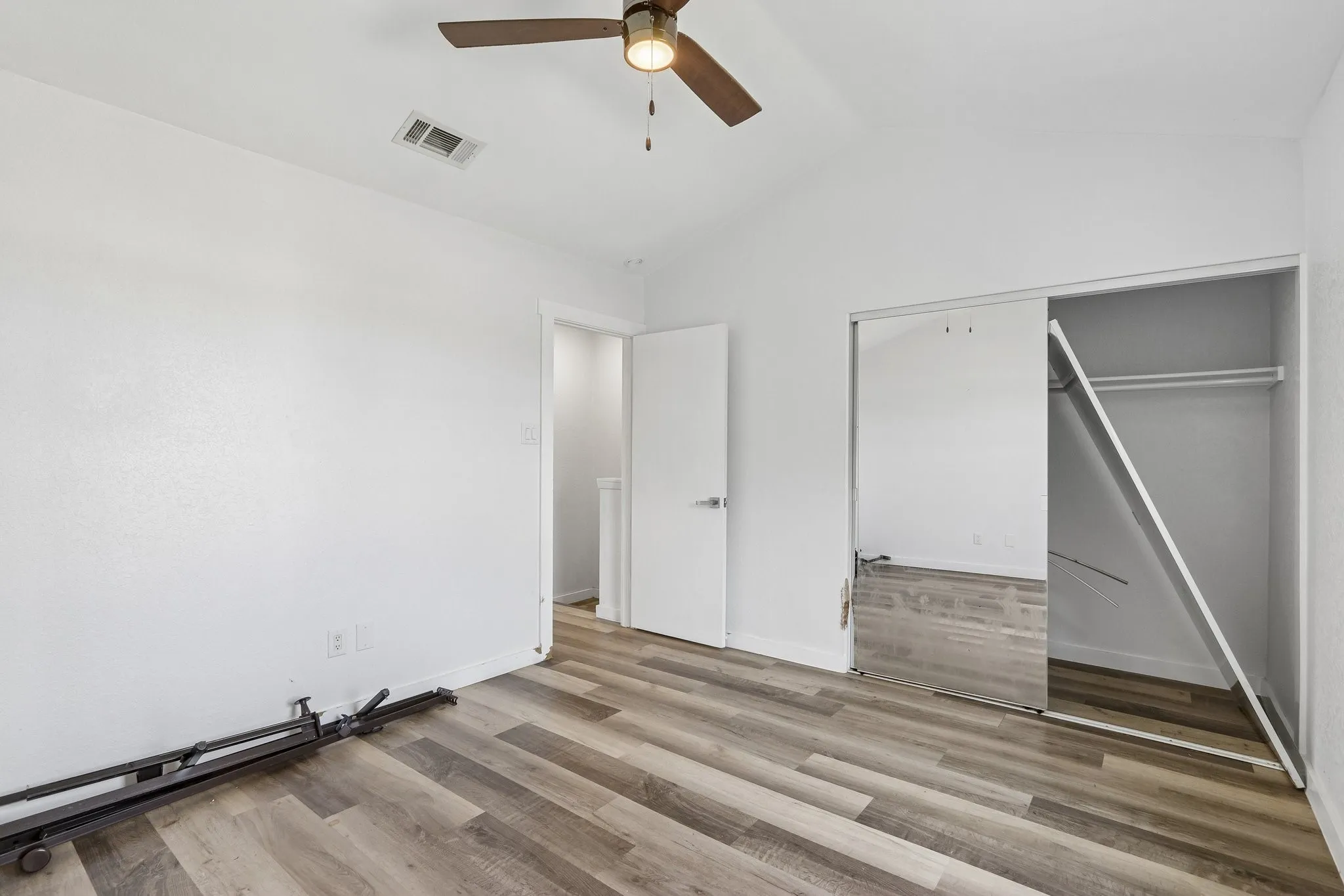 Spacious room featuring vaulted ceilings, wood-finish flooring, a ceiling fan with integrated lighting, and a mirrored sliding closet door
