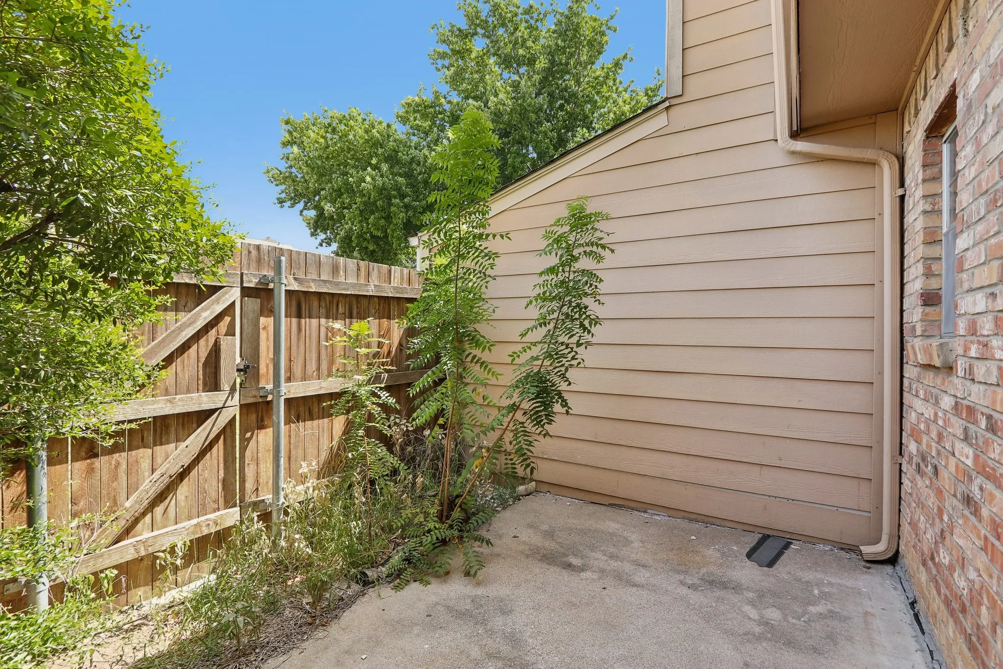 Exterior featuring a wooden privacy fence, a concrete patio area, tan horizontal siding, and a brick wall