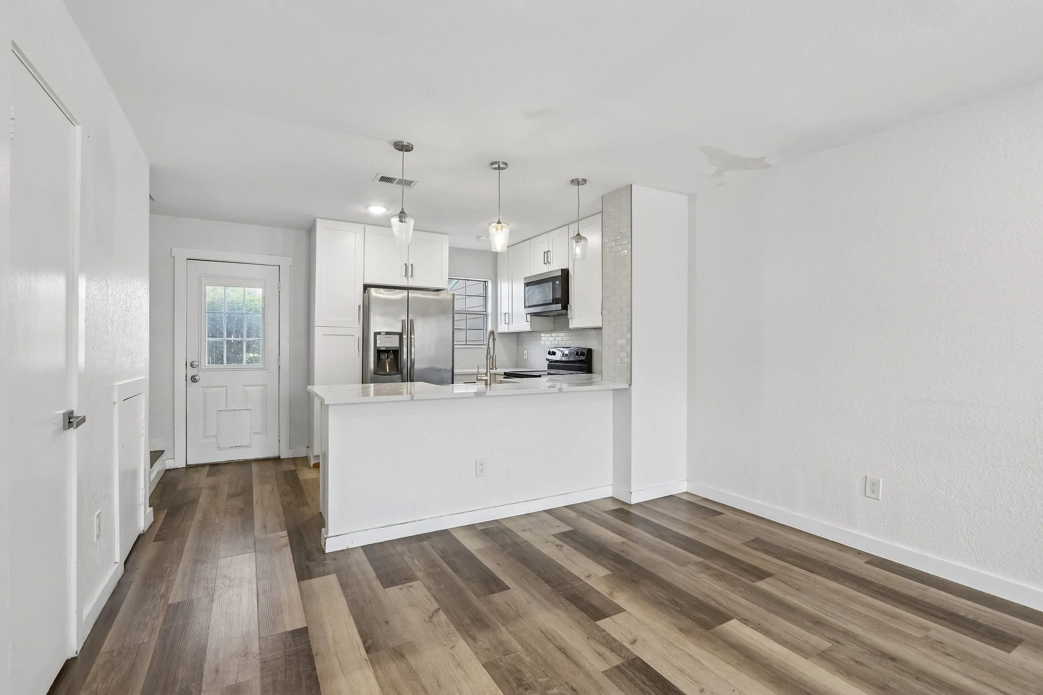 Open-concept living space featuring wood-finish flooring, a contemporary kitchen with white cabinetry, stainless steel appliances, a breakfast bar, and pendant lighting
