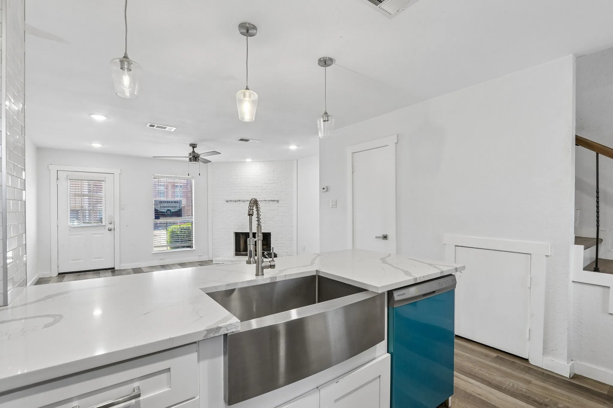 Kitchen island featuring a farmhouse-style stainless steel sink, a pull-down faucet, and white countertops with veining