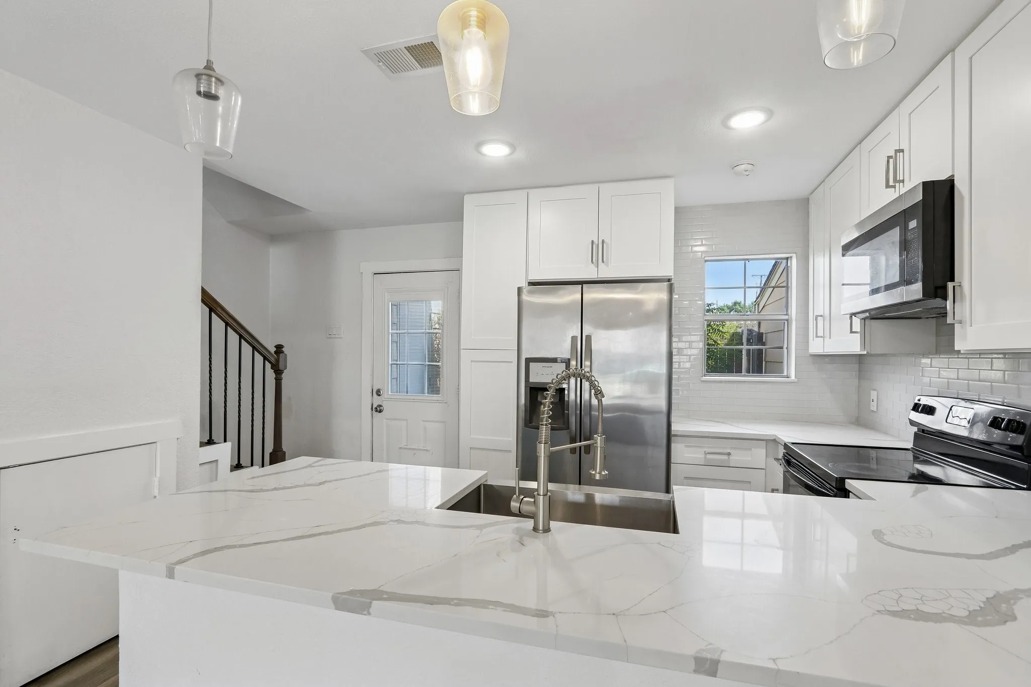 Modern kitchen featuring white shaker cabinetry, stainless steel appliances, a subway tile backsplash, white countertops, and a kitchen island with an integrated sink and faucet