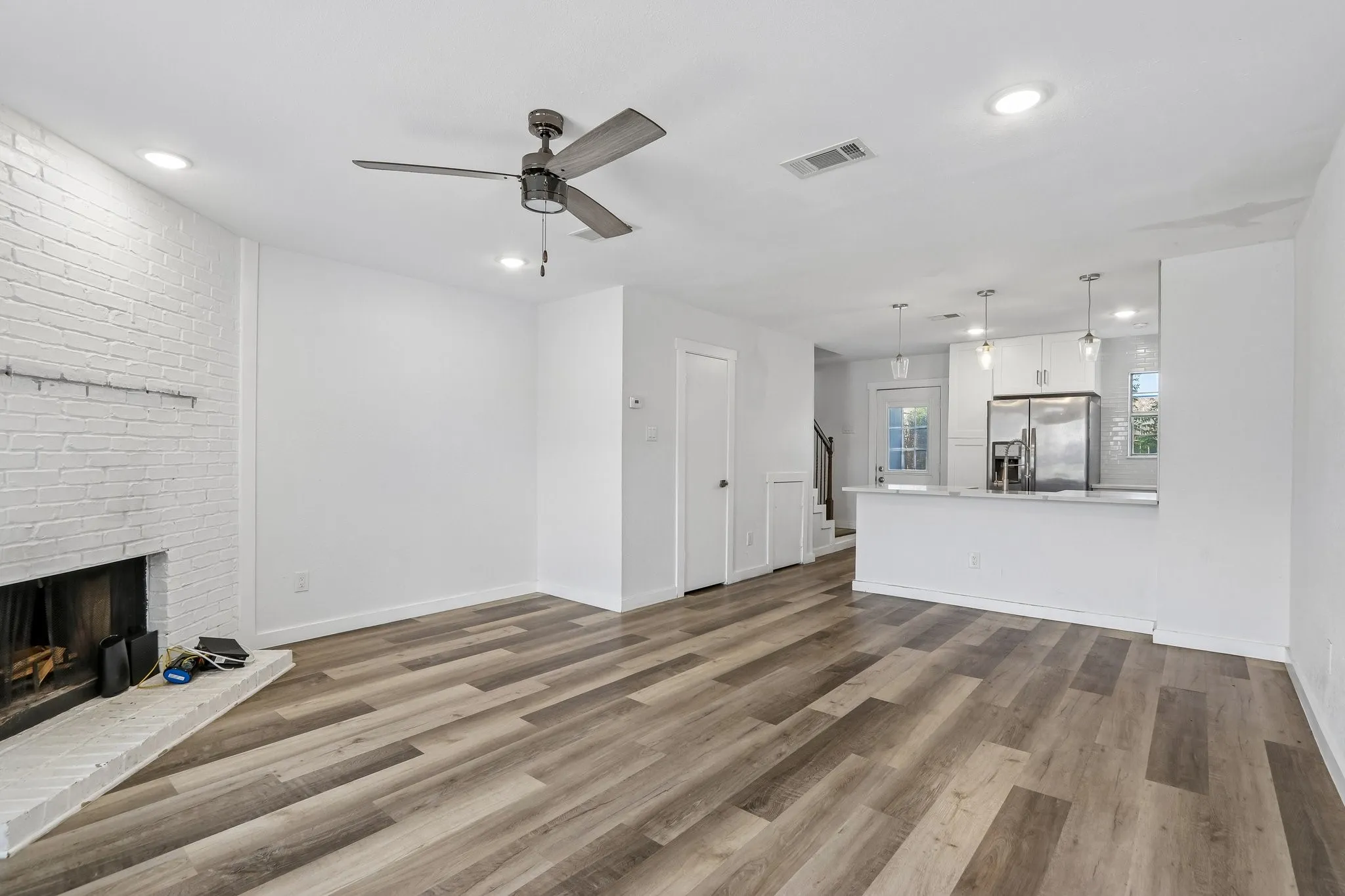 Open-concept living area featuring wood-finish flooring, a painted brick fireplace, and recessed lighting