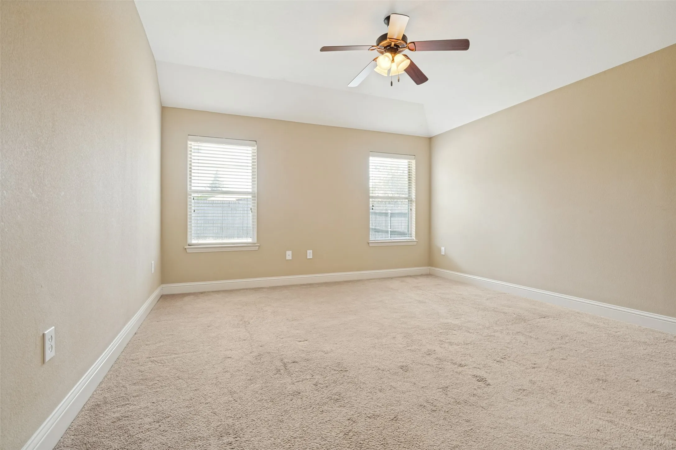 Spacious room featuring neutral carpeting, light beige walls, a tray ceiling, and a ceiling fan