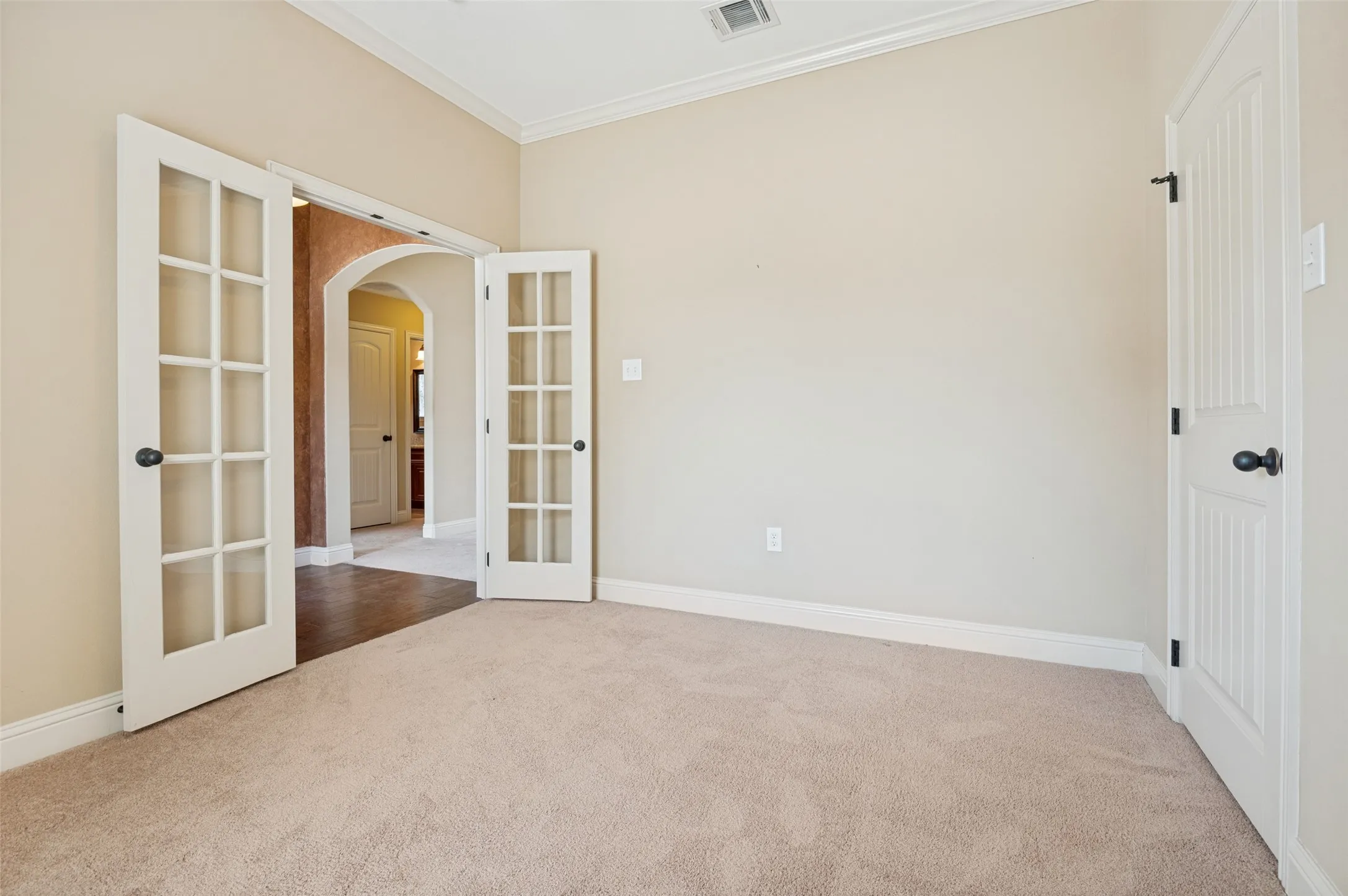 Room featuring double French doors with grid-patterned glass, neutral-toned walls, and plush carpeting