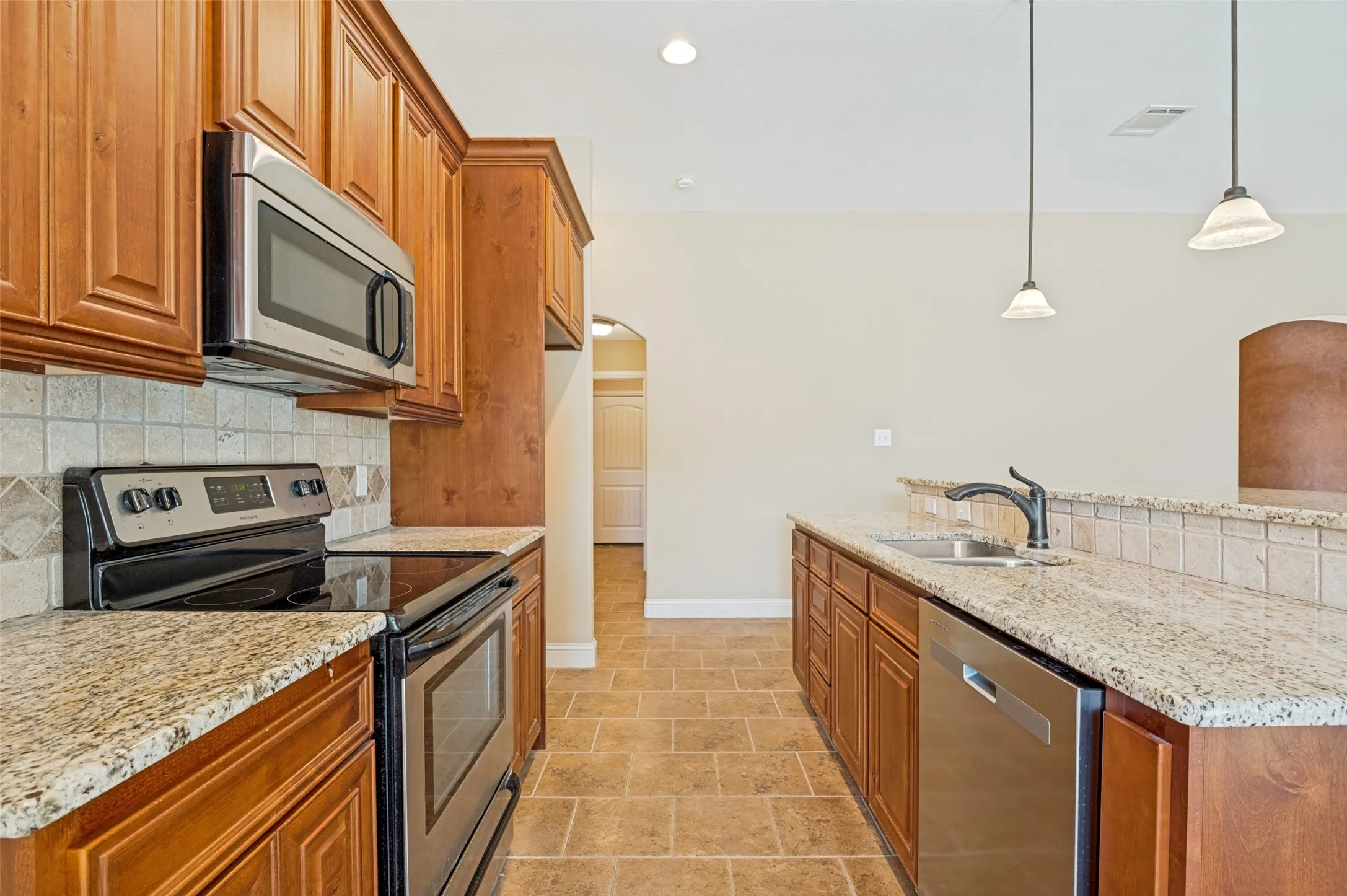 Kitchen featuring wood cabinetry, stainless steel appliances, speckled stone countertops, and a tile backsplash