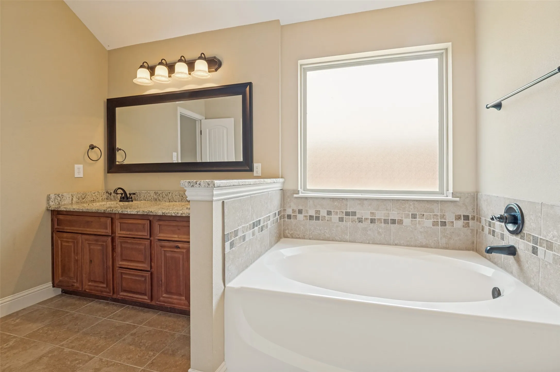 Soaking tub with a tiled surround featuring a decorative mosaic band