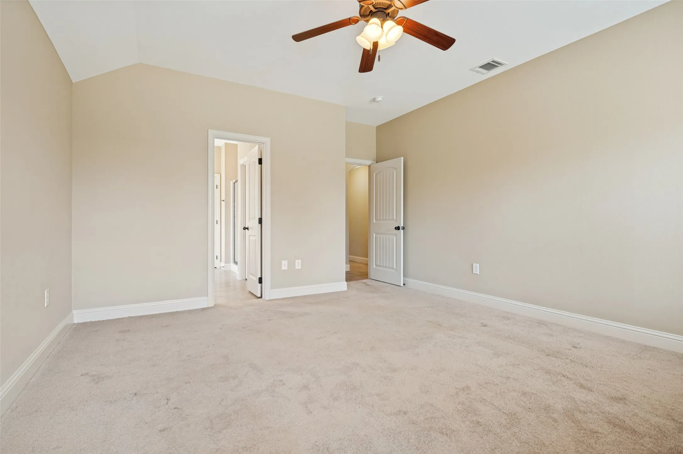 Spacious room featuring vaulted ceilings, neutral-toned carpeting, a ceiling fan with integrated lighting, and white baseboards