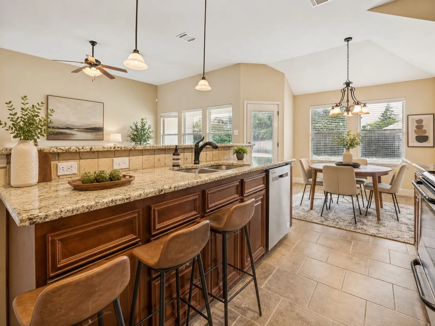 Kitchen featuring granite countertops, wood cabinetry, stainless steel dishwasher, tile flooring, and a dining area with ample natural light