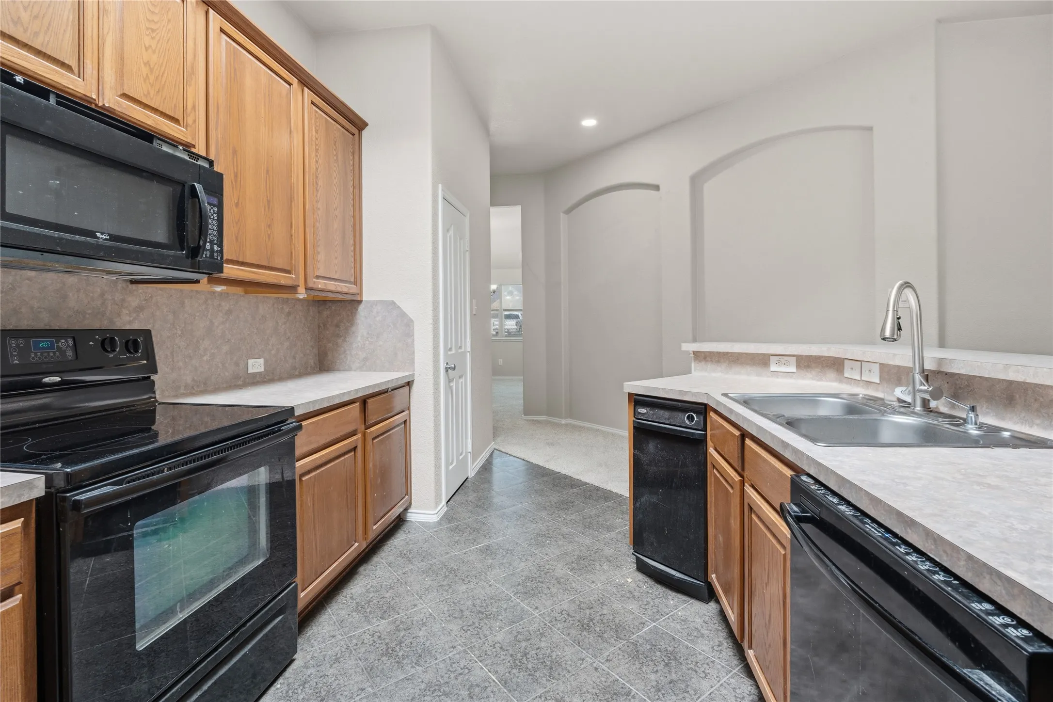 Kitchen featuring ample wood cabinetry, black appliances including an oven and microwave, a double basin stainless steel sink with a gooseneck faucet, and tile flooring