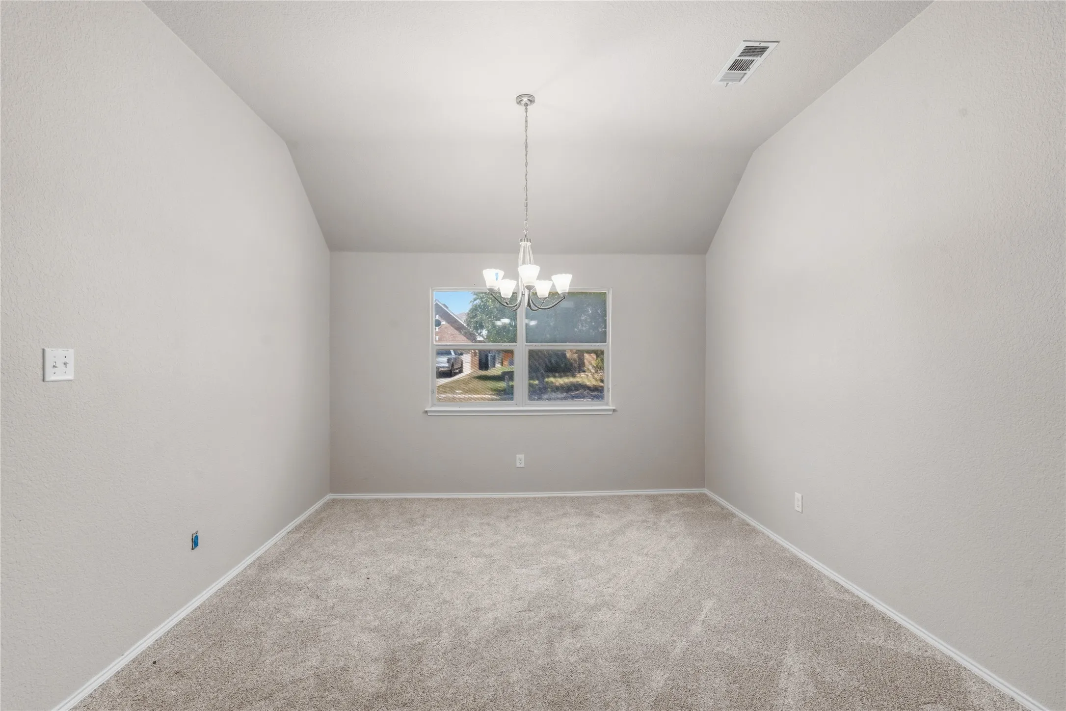 Carpeted interior space featuring a window with a street view, a vaulted ceiling, a hanging chandelier, and white baseboards