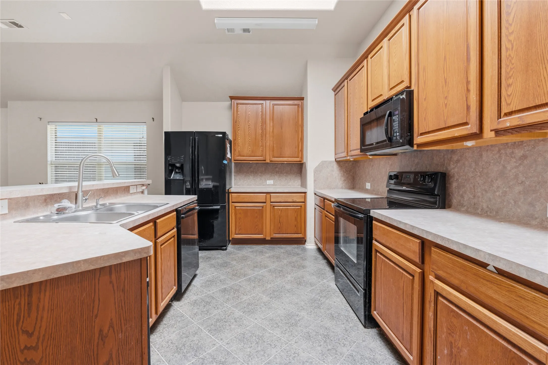 Kitchen featuring warm wood cabinetry, neutral countertops, and black appliances