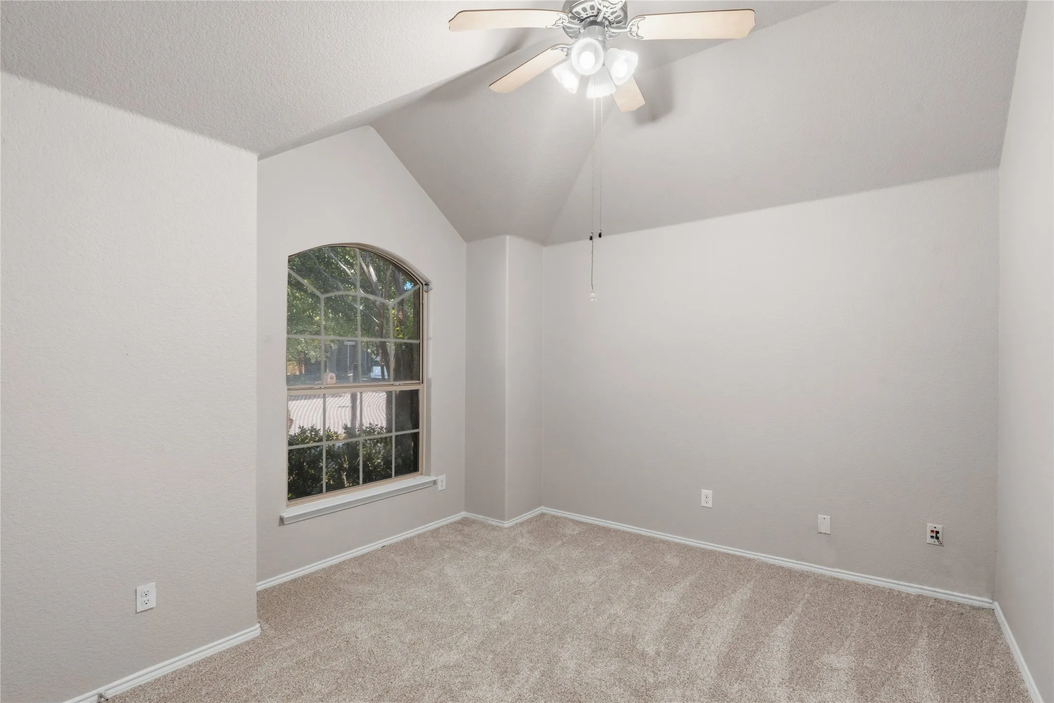 Vaulted ceiling room featuring light-colored carpeting and a distinctive arched window
