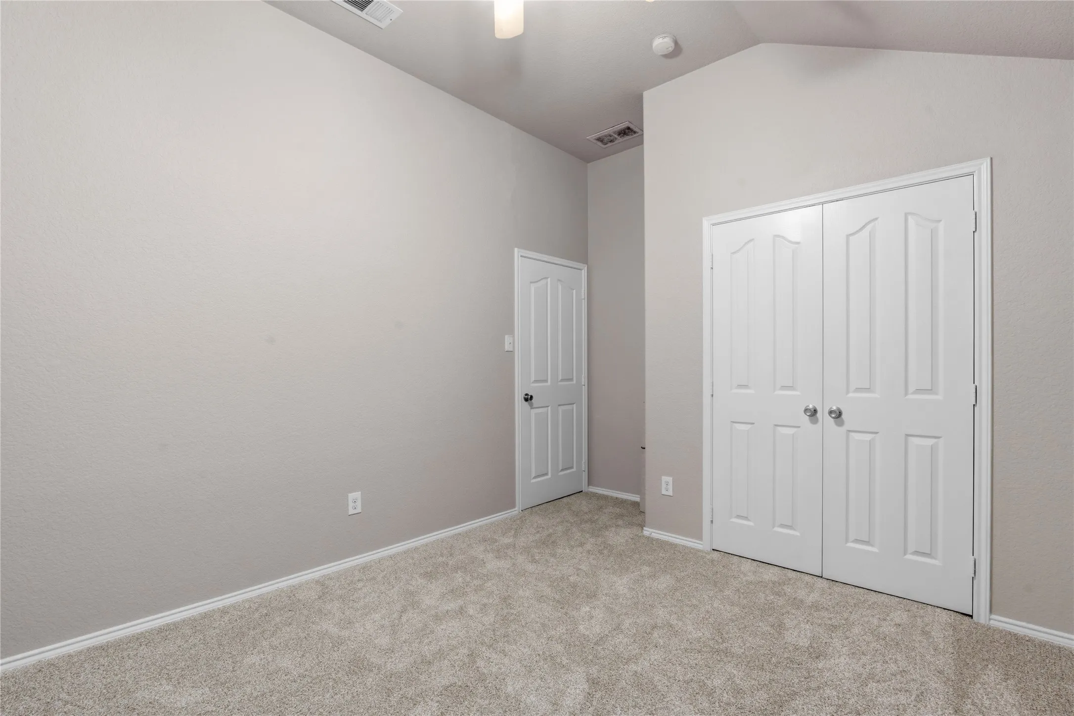 Spacious room featuring vaulted ceilings, neutral-toned carpeting, and a ceiling fan