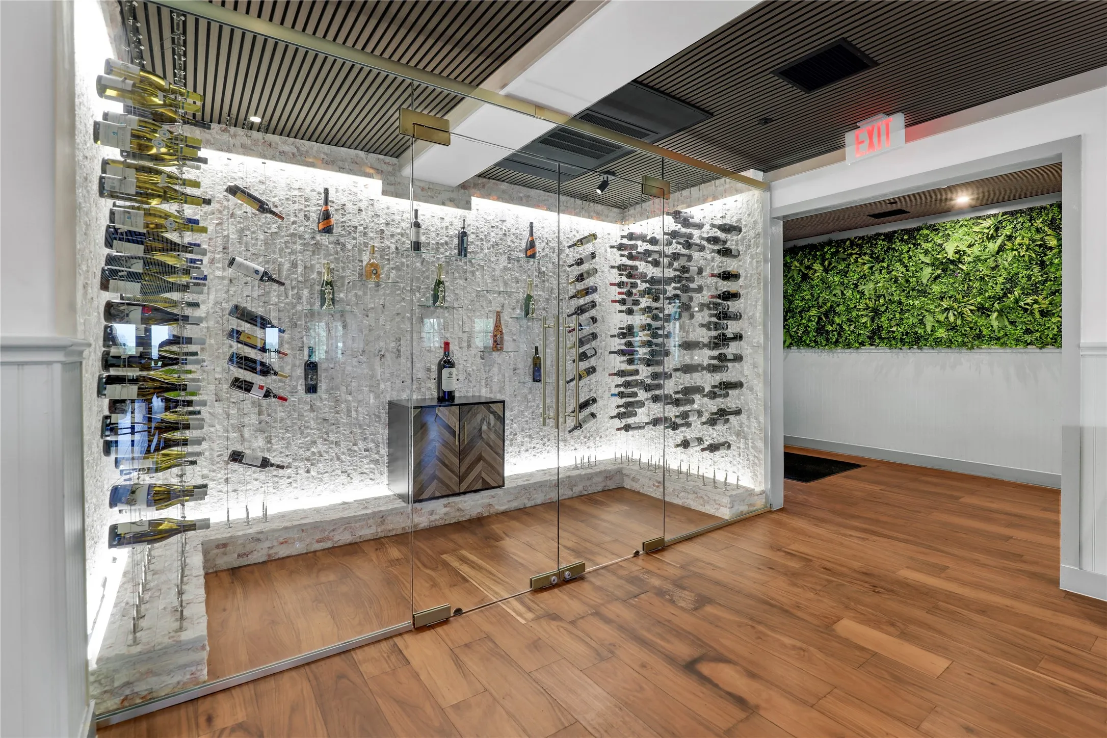 Glass-enclosed wine cellar featuring back-lit stone walls, integrated bottle racking, and a built-in wood-finish cabinet