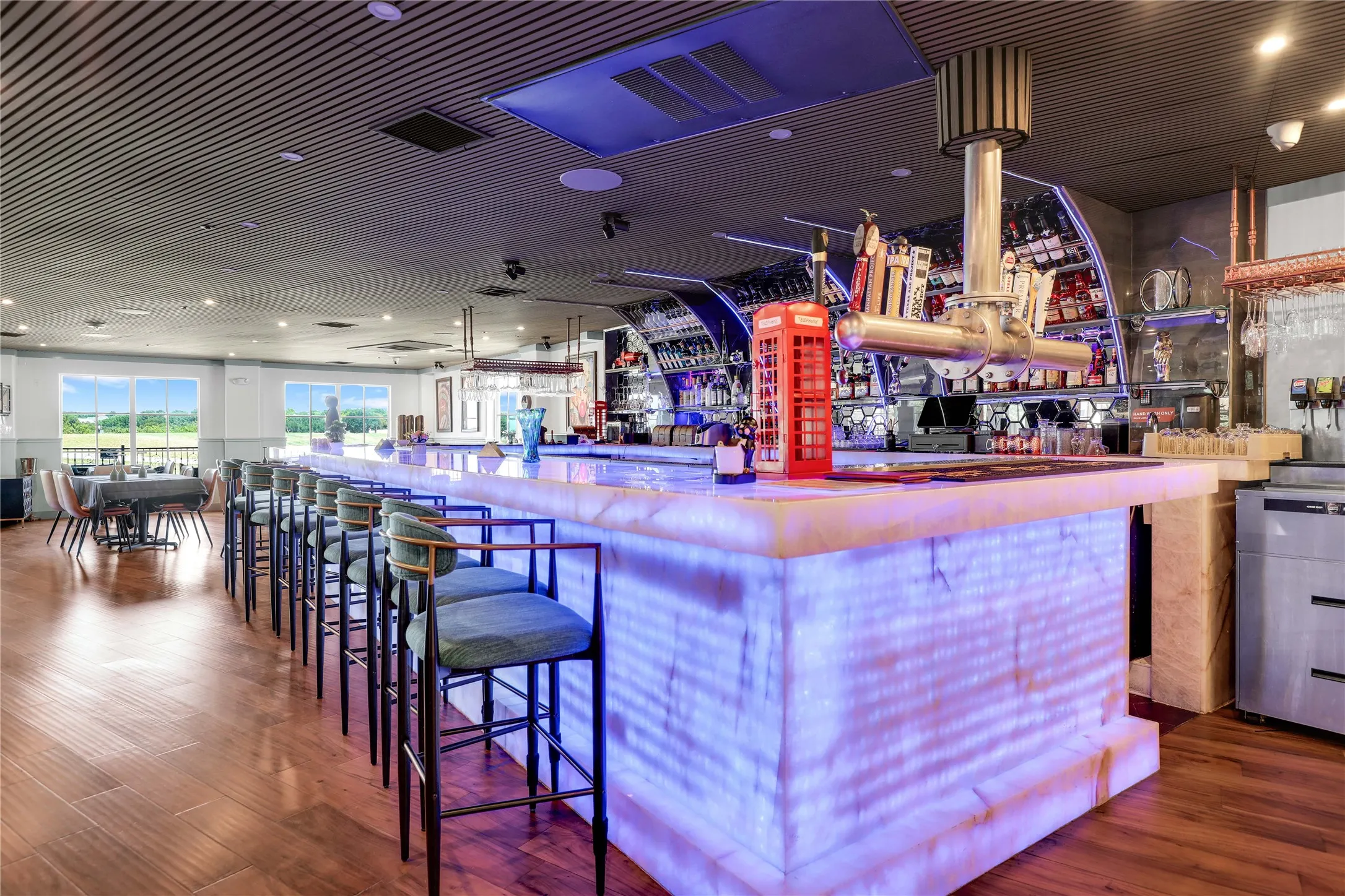 Illuminated bar with multiple taps and bottle storage, featuring an elongated countertop with seating for multiple patrons