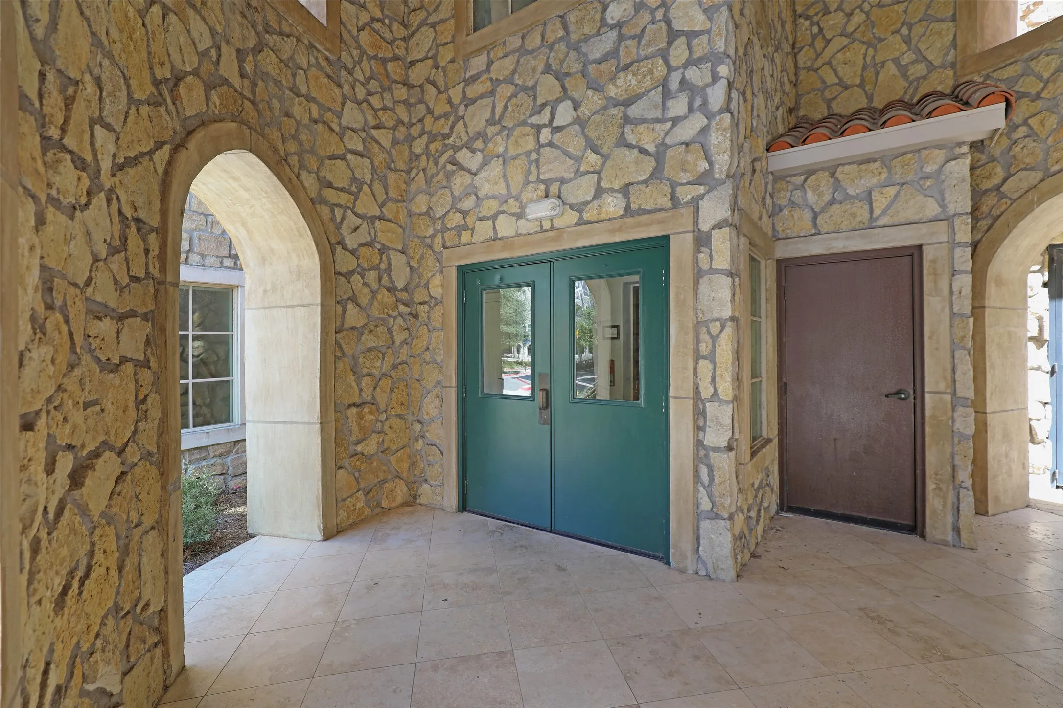 Exterior stone facade featuring multiple arched entries and a covered patio with tiled flooring