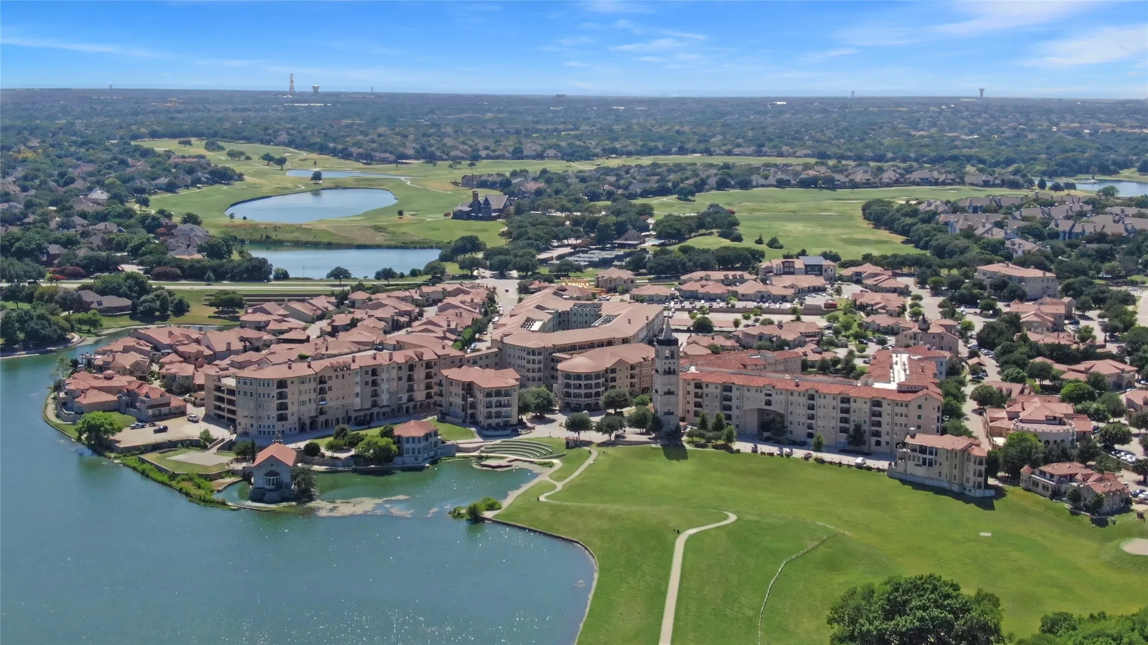 Aerial overview featuring a community with Mediterranean-style architecture, red tile roofs, and stucco exteriors situated around a body of water