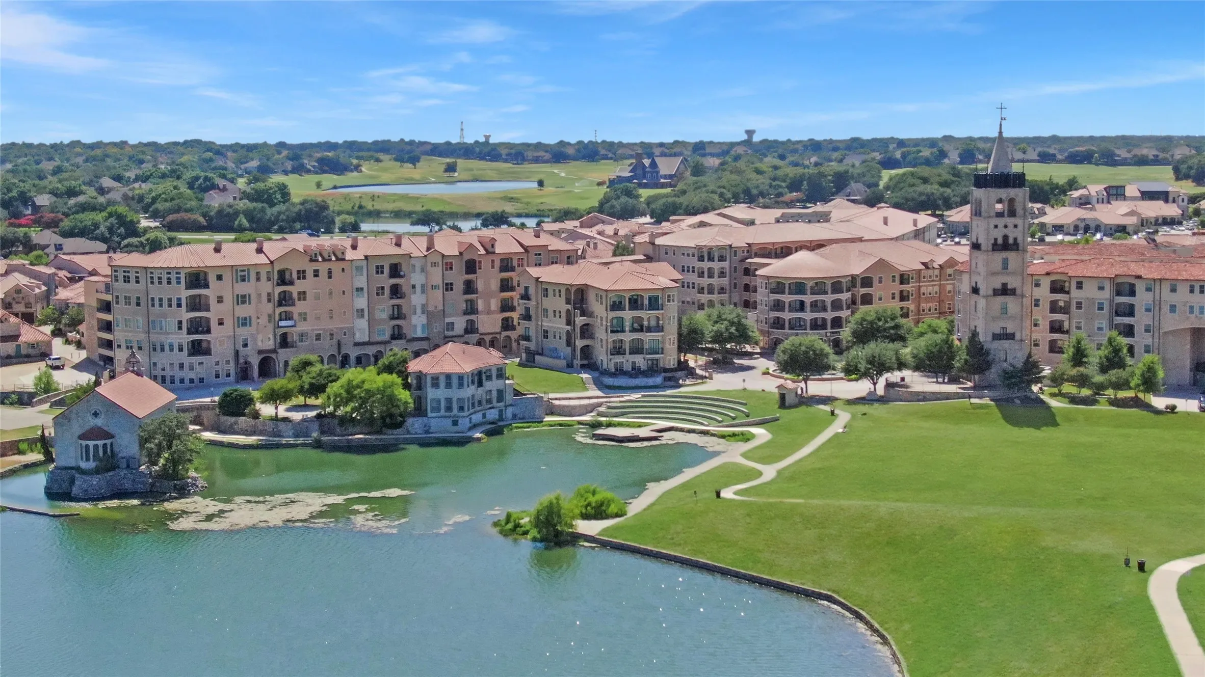 Waterfront community featuring multi-story buildings with balconies, a prominent bell tower, and a manicured green space