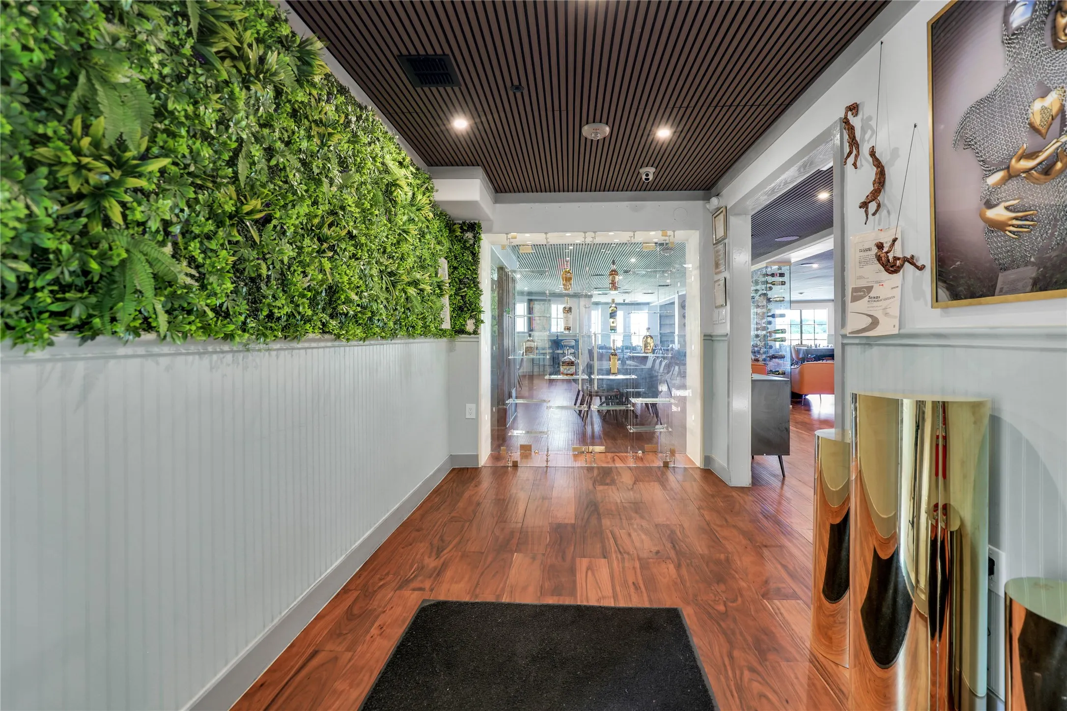 Entryway featuring a striking green wall installation, wood-finish flooring, white wainscoting, and a slatted ceiling