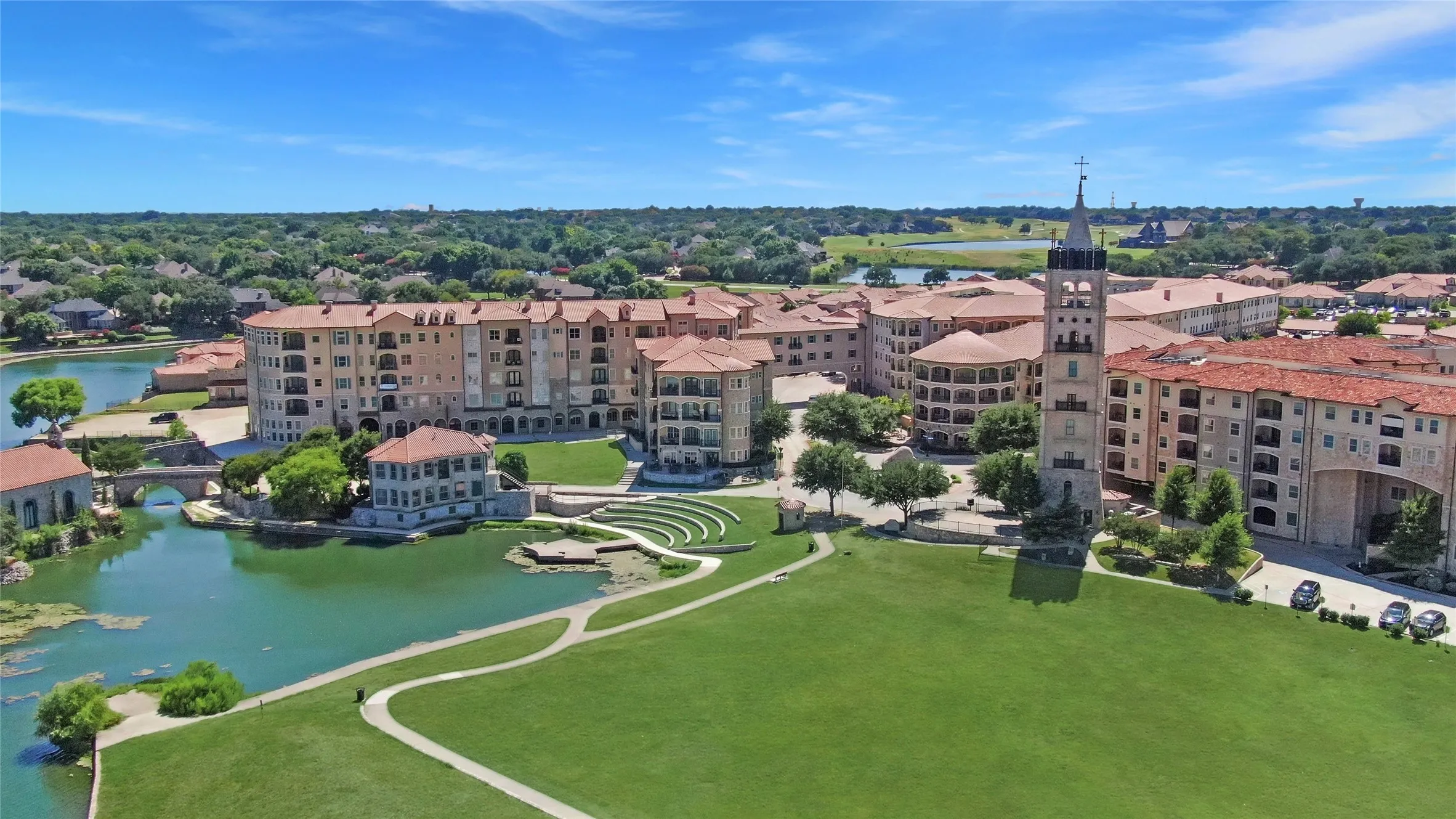 Expansive green space bordered by a multi-story building complex featuring balconies, red tile roofs, and stone facades