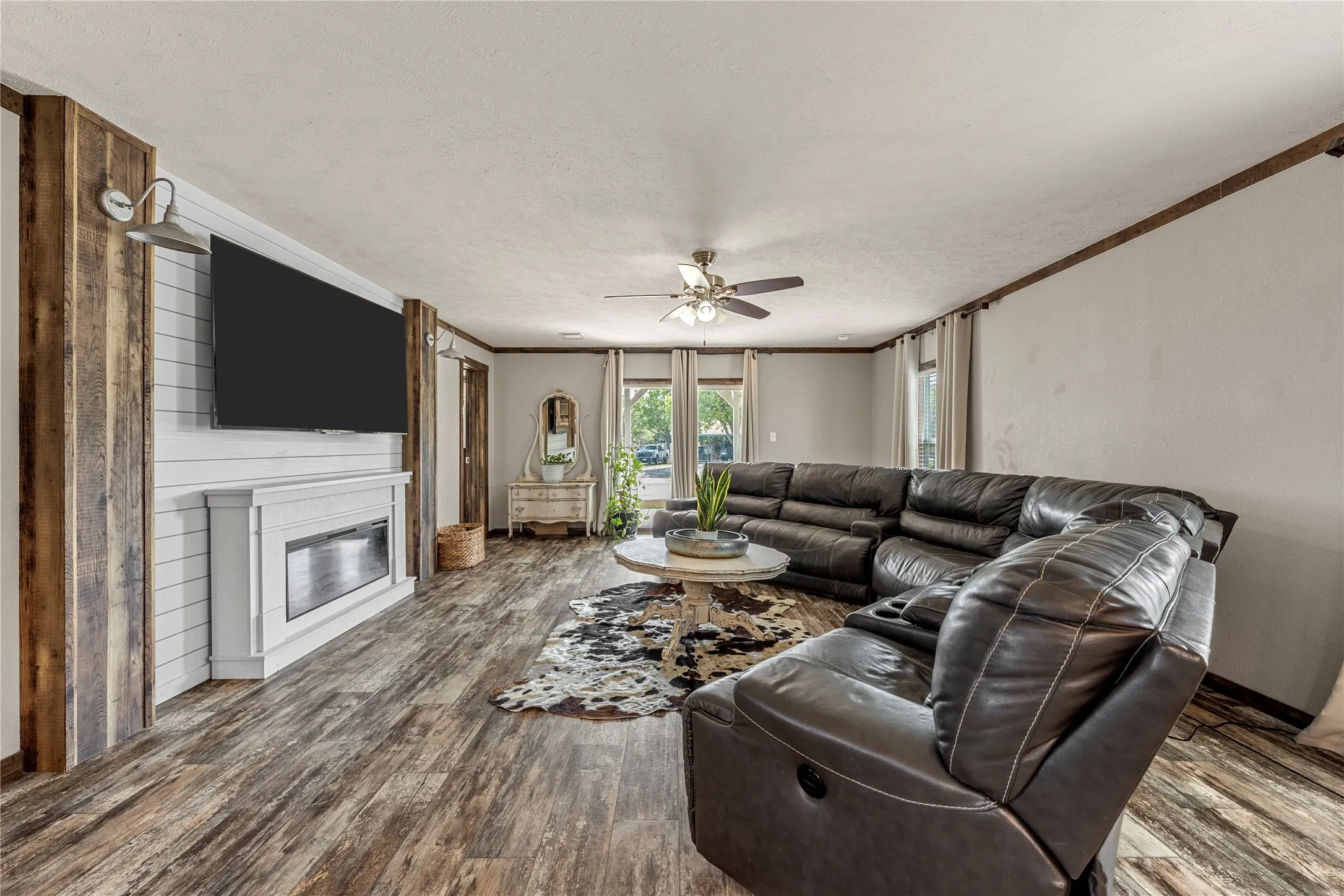 Living area featuring wood-finish flooring, an electric fireplace with a shiplap surround, and an overhead ceiling fan