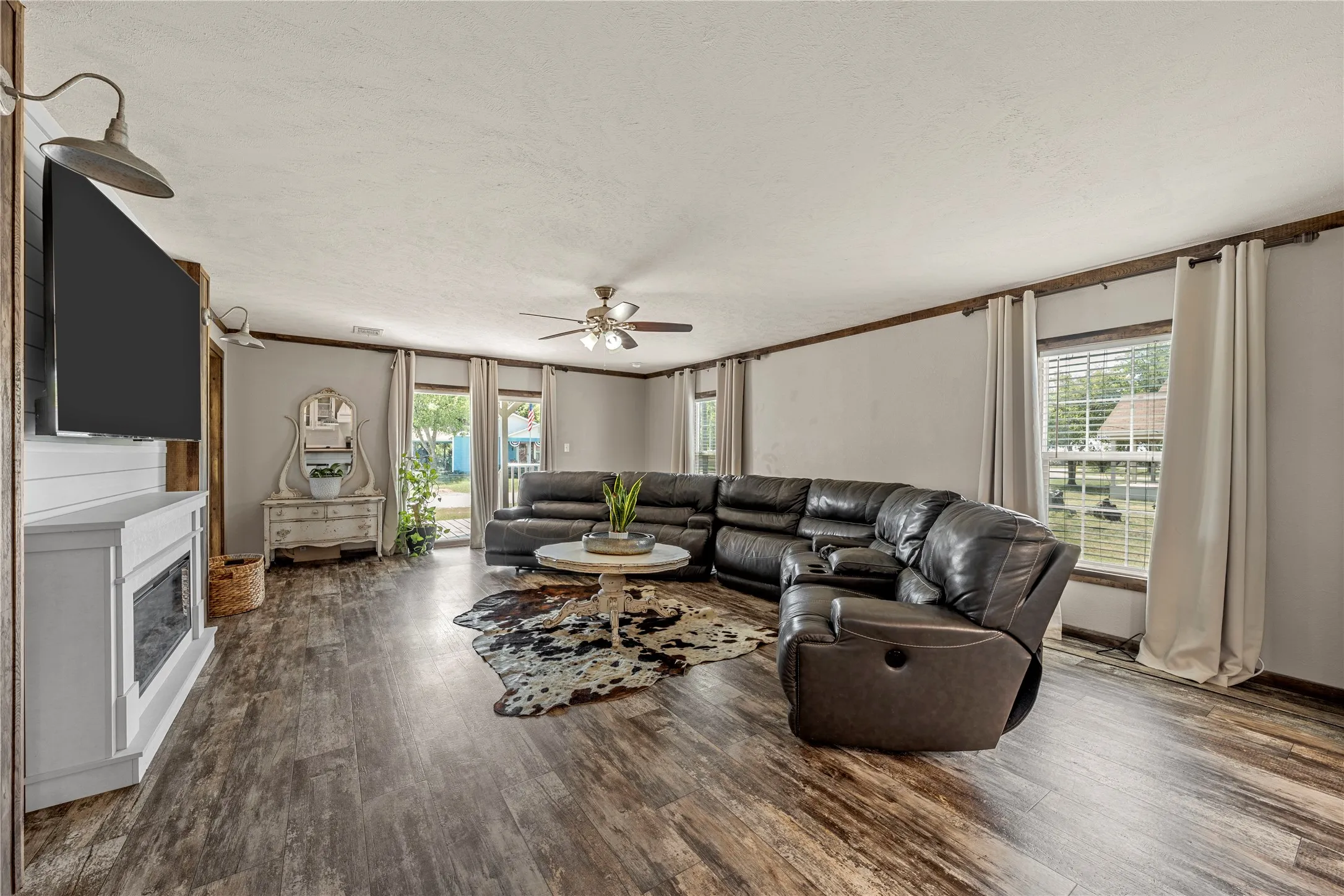 Spacious living area featuring wood-finish flooring, a ceiling fan, and multiple windows with blinds and curtain rods