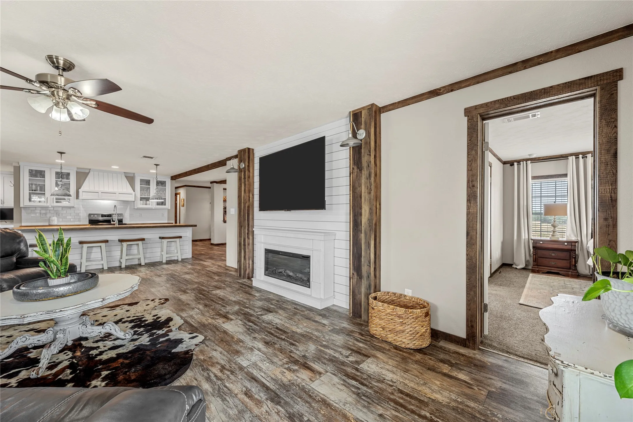 Open-concept living area featuring wood-finish flooring, a contemporary fireplace with shiplap surround, and exposed wood beams