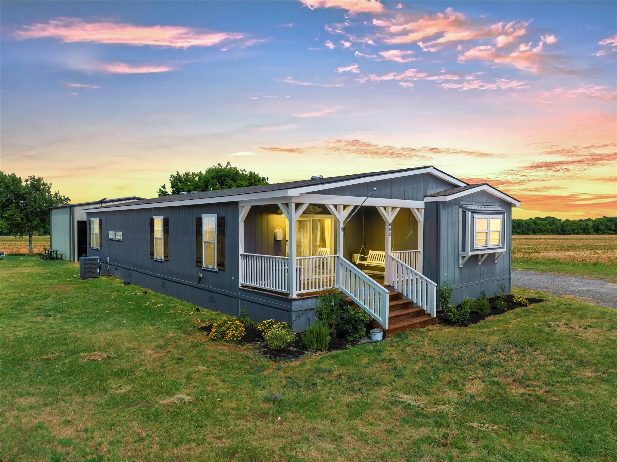 Contemporary home featuring dark siding, a covered porch with white railings, and a side-mounted HVAC unit