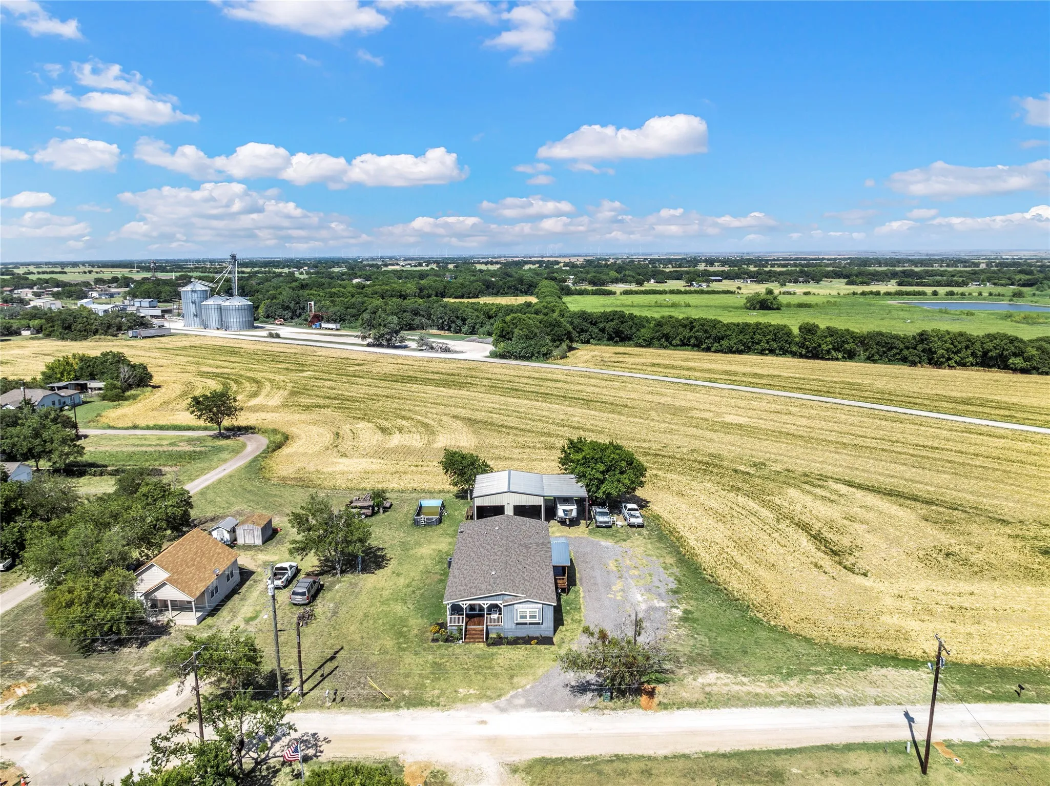 Expansive rural property featuring a main residence with a covered front porch, a separate guest house, a detached garage structure, and an agricultural field