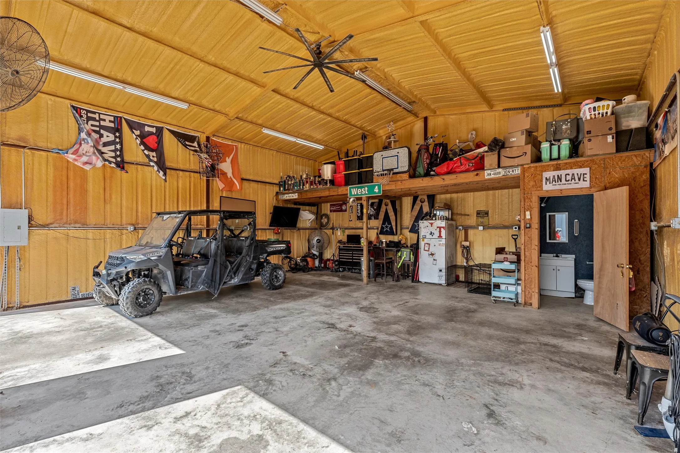 Spacious garage with concrete flooring and insulated walls, featuring a large ceiling fan, overhead lighting, and an integrated loft storage area