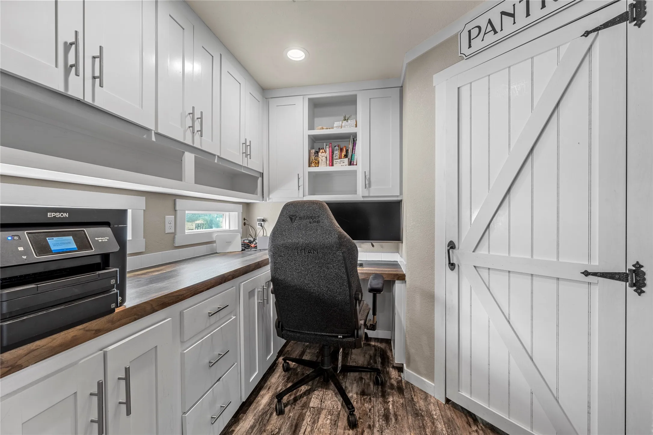 Dedicated workspace featuring extensive white cabinetry, a wood-finish countertop, and wood-finish flooring
