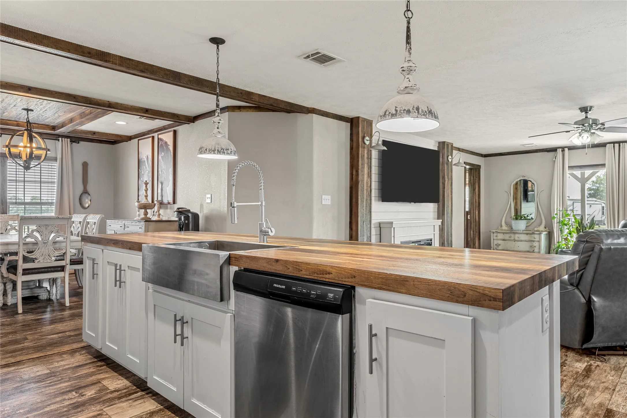 Kitchen island featuring a wood-finish countertop, stainless steel farmhouse sink, and integrated dishwasher