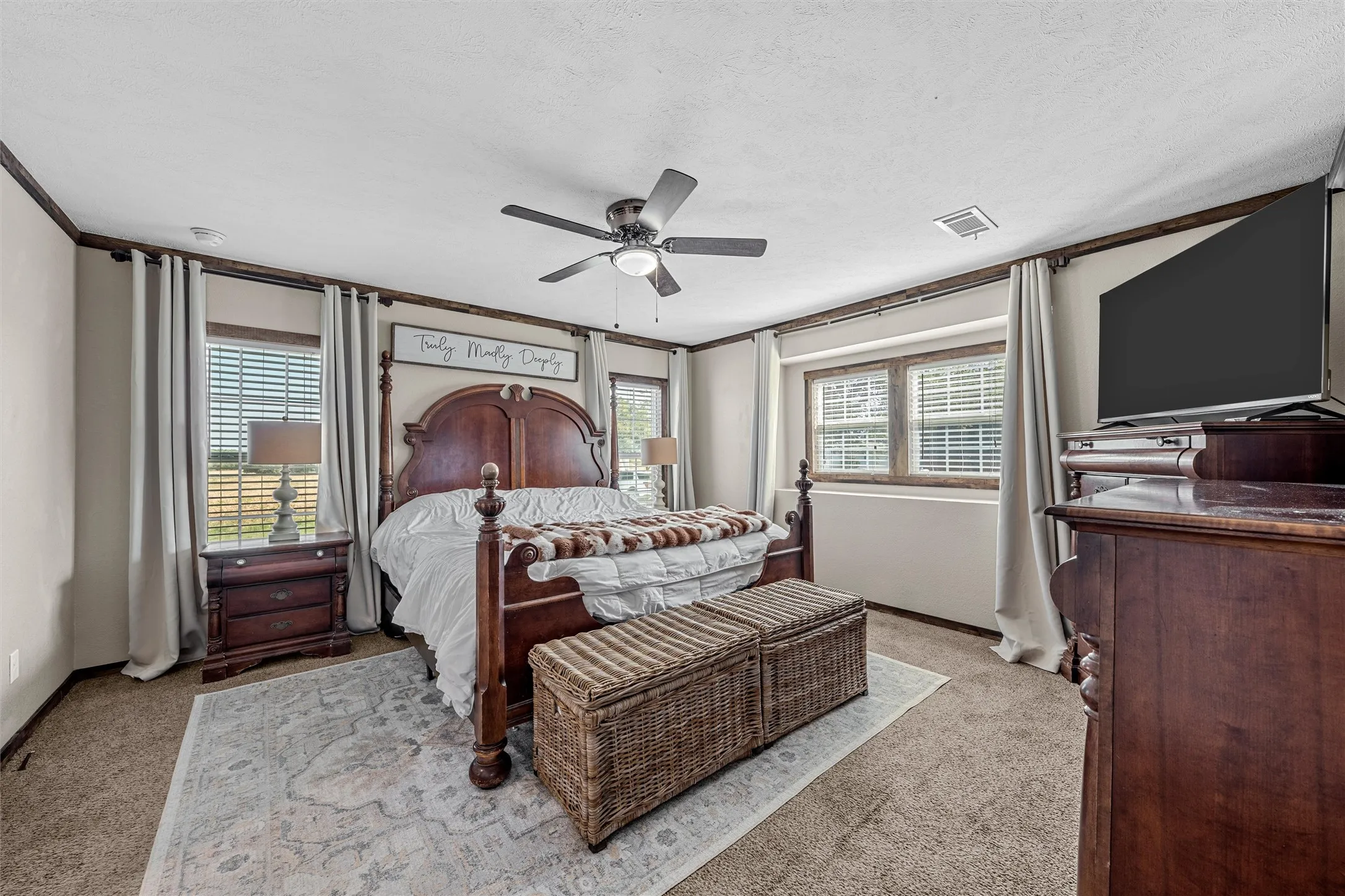 Carpeted room featuring multiple windows with blinds, a ceiling fan, and decorative trim
