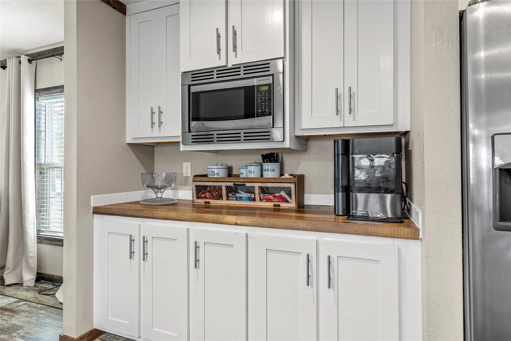 Galley kitchen with white shaker-style cabinetry, wood-finish countertops, and a built-in stainless steel microwave