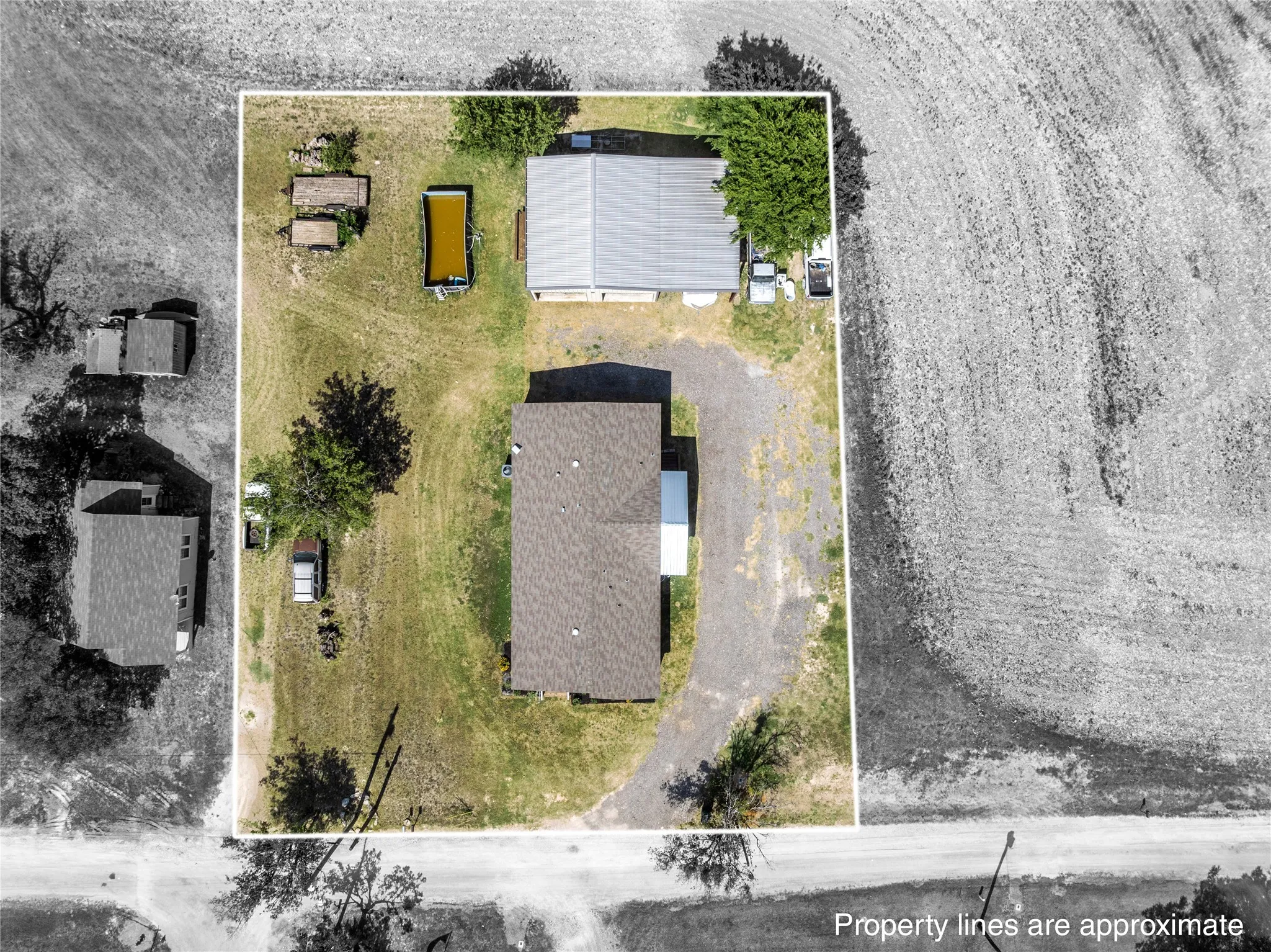 Aerial view of a rectangular property featuring a primary residence with a dark shingle roof and a separate outbuilding with a metal roof