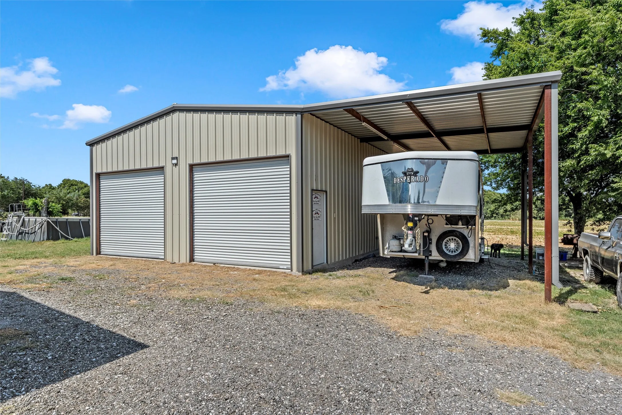 Metal-sided structure featuring two roll-up doors, exterior lighting, and an attached covered carport