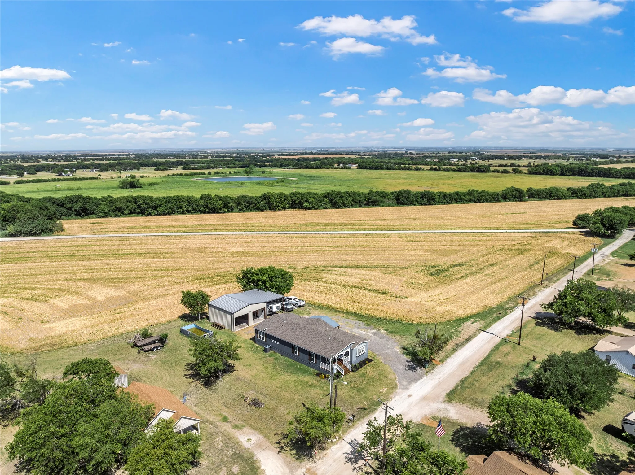 Rural property featuring a single-story dwelling, a large detached metal building, and expansive surrounding fields