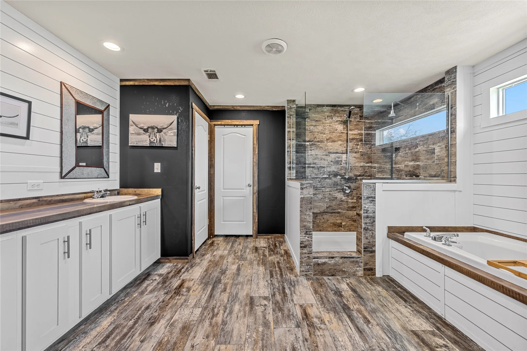 Bathroom featuring wood-finish flooring, a freestanding soaking tub, a walk-in shower with glass enclosure, a vanity with a countertop, and horizontal paneling