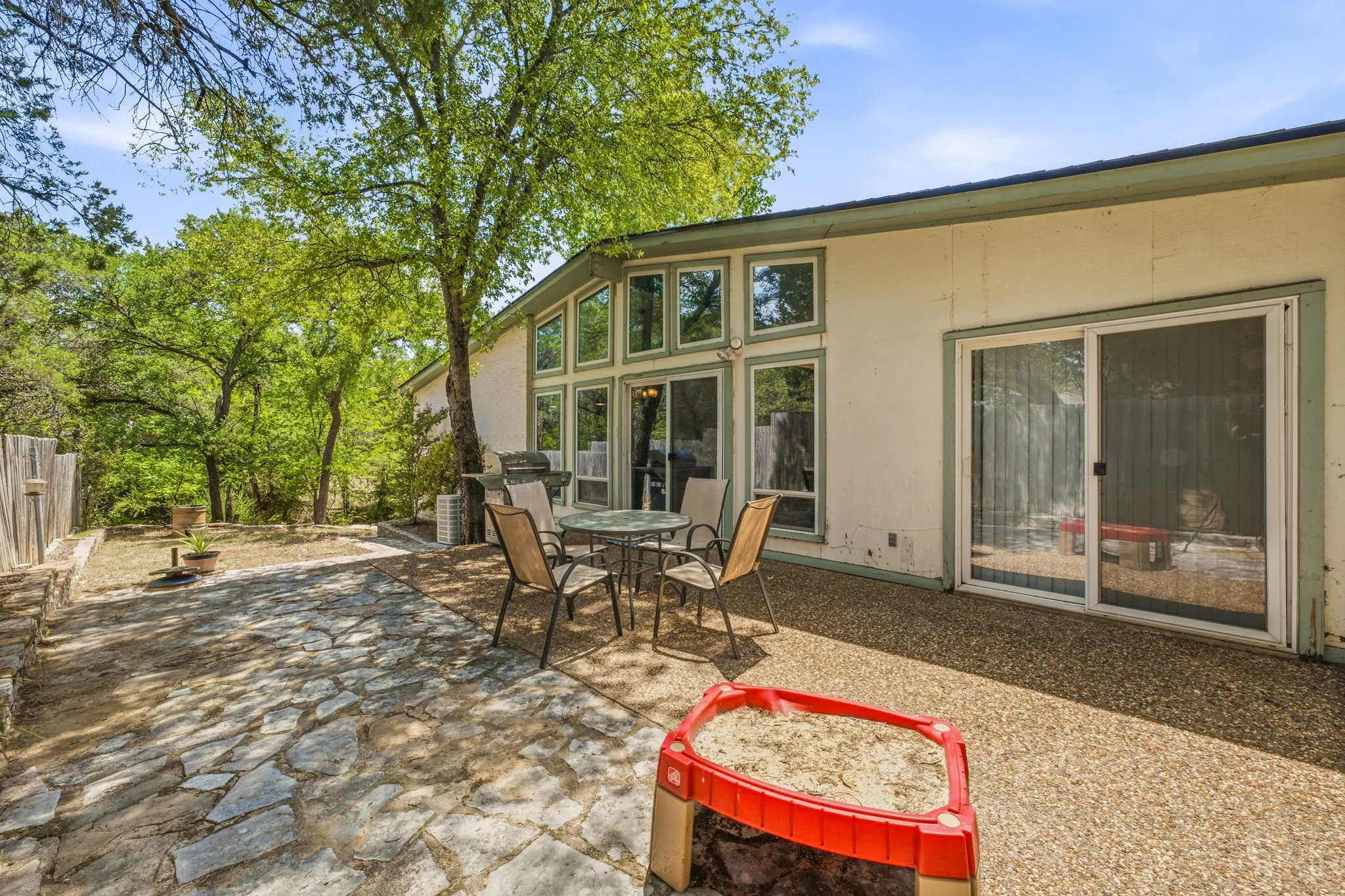 Expansive outdoor living area featuring a flagstone patio, an additional aggregate patio, and mature trees providing natural shade