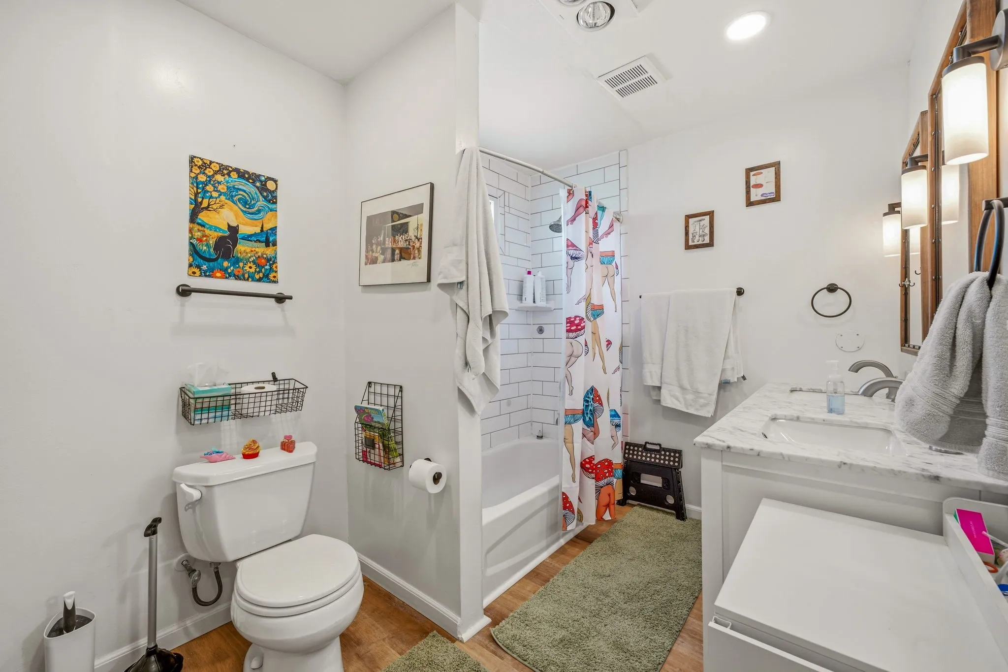 Bathroom featuring a white subway tile shower surround, a white vanity with a light-toned countertop, and wood-finish flooring