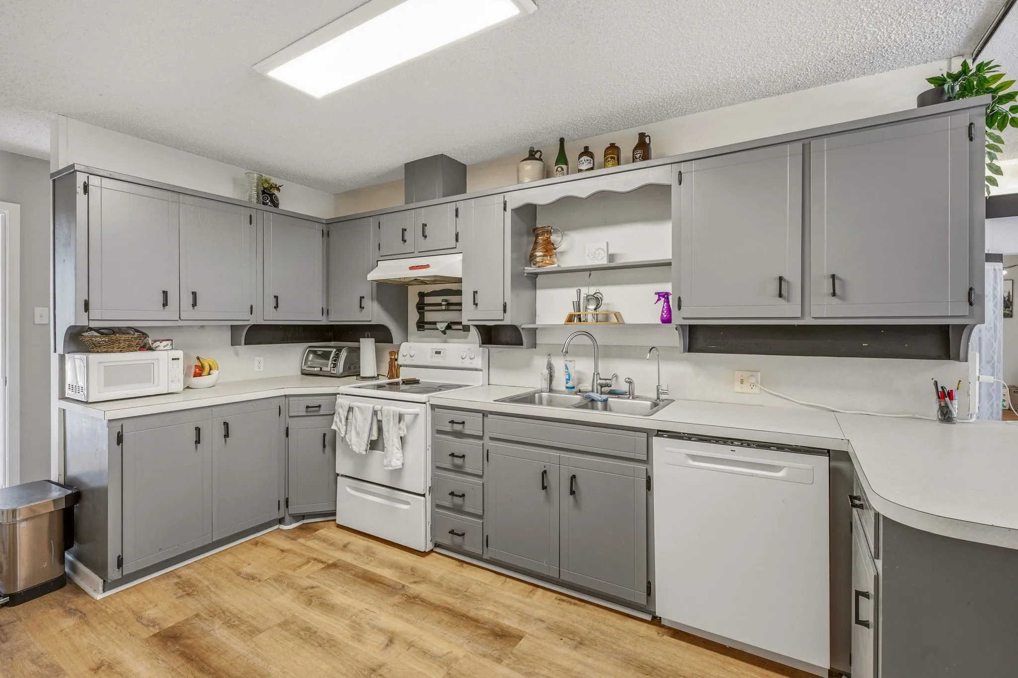 Kitchen featuring wood-finish flooring, light gray cabinetry with black hardware, white countertops, and a white oven