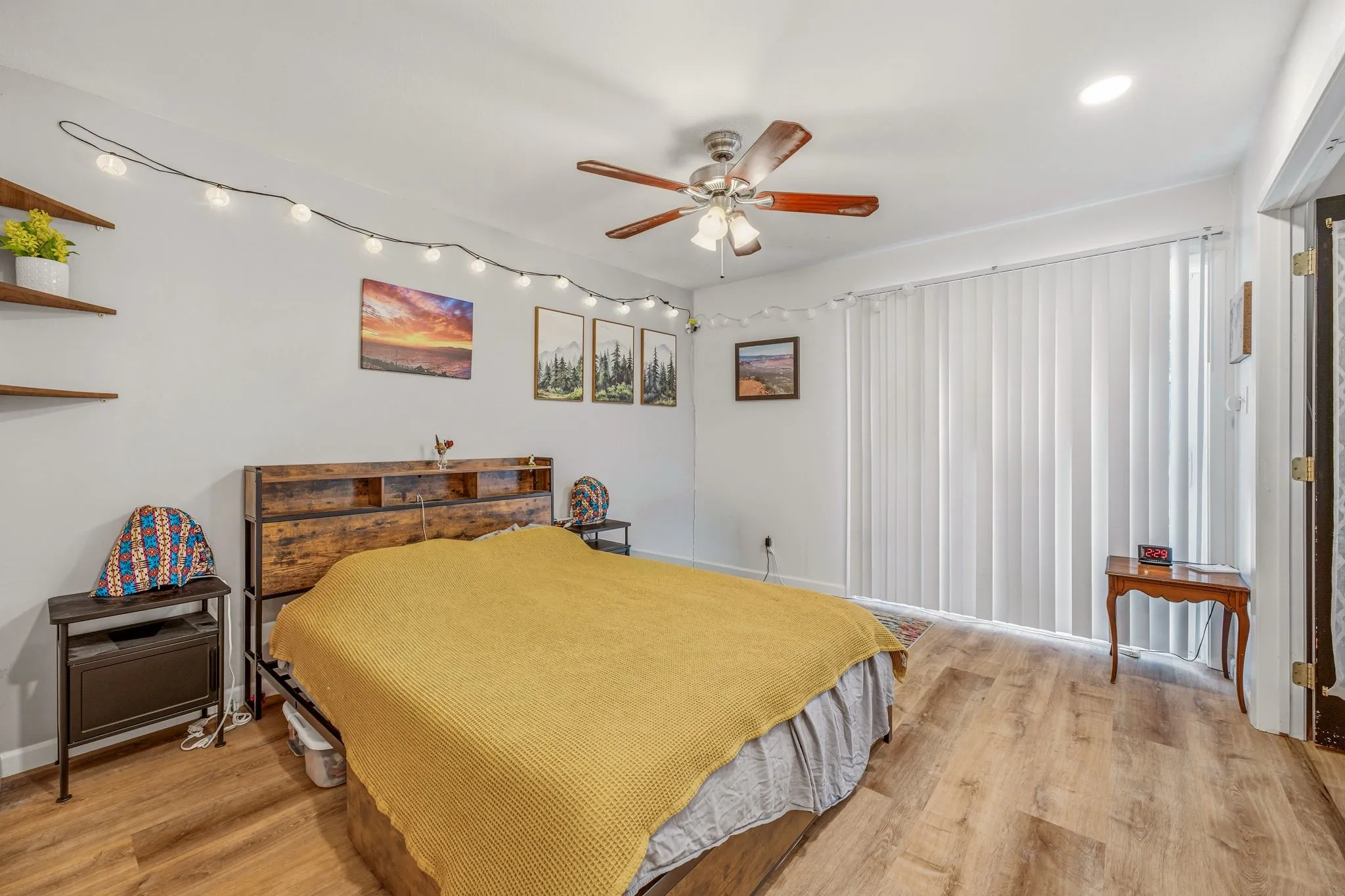 Room featuring wood-finish flooring, a ceiling fan with integrated lighting, and vertical blinds covering a large window